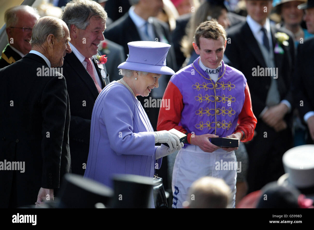 Königin Elizabeth II. Und der Herzog von Edinburgh und der siegreiche Jockey Ryan Moore, nachdem ihr Pferd Estimate am vierten Tag des Royal Ascot-Treffens 2012 auf der Ascot Racecourse, Berkshire, die Vase der Königin gewonnen hatte. Stockfoto