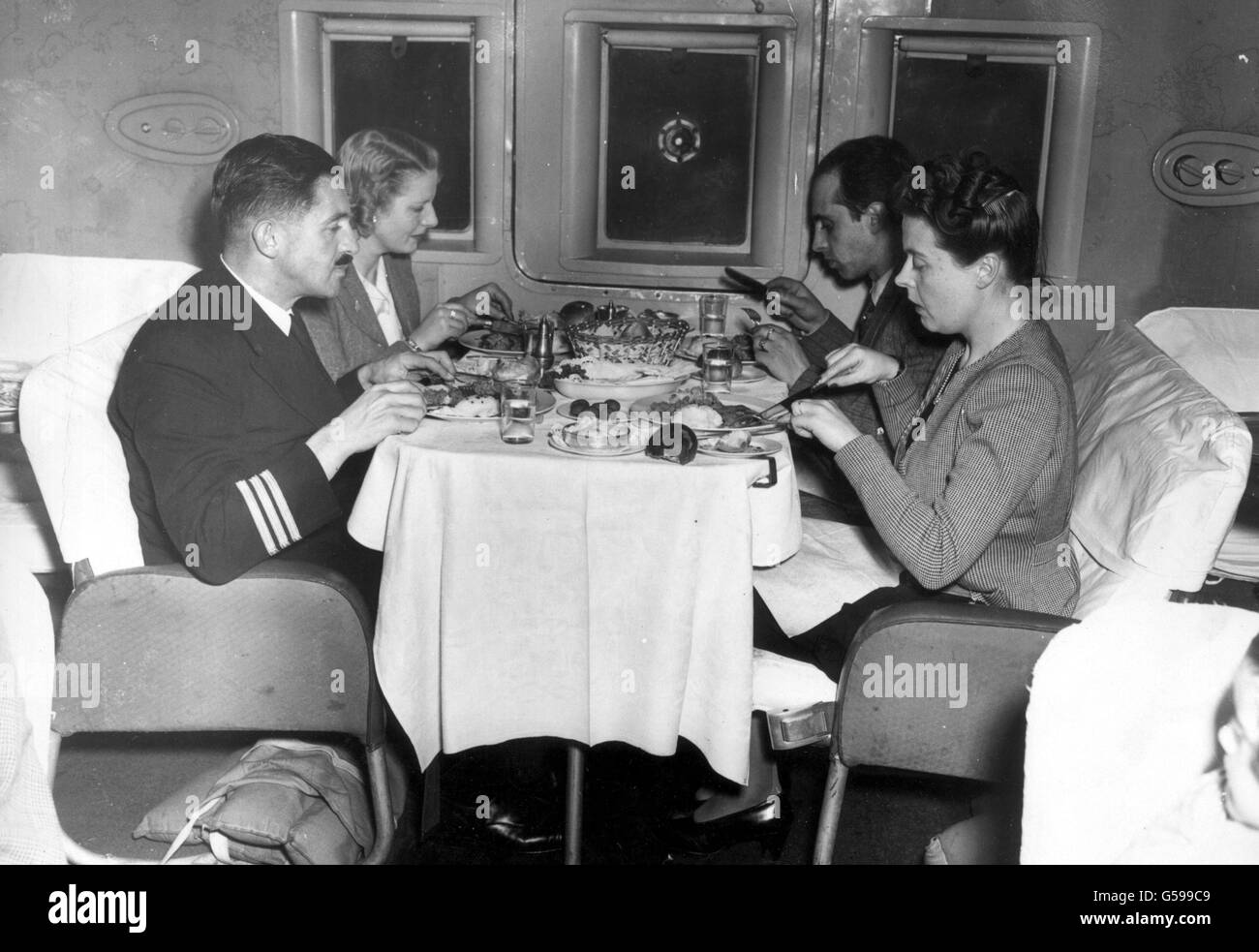 Ein Kapitän eines fliegenden Bootes, der mit Passagieren speist, wenn er sich Lissabon nähert, auf dem Weg nach Amerika. Sie genießen ein warmes drei-Gänge-Abendessen, das einige Tage gekocht und gefroren wurde, bevor es in eine spezielle Heizung gestellt und heiß serviert wurde. *Passagiere auf Empire-Langstreckenflügen werden bald vier-Gänge-Menüs genießen, die 10 000 Meter über dem Mittelmeer oder dem Persischen Golf serviert werden. In einer speziell ausgestatteten Londoner Küche führen die Experten von BOAC Experimente mit neuartigen "Tiefgefriermethoden" durch. Sie zielen auf Perfektion im Vorgaren, Verpacken und Gefrieren bei außergewöhnlich niedrigen Temperaturen, BOAC Stockfoto