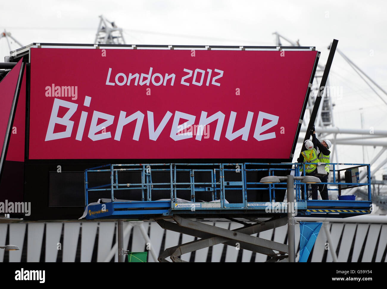 Olympische Spiele - Olympische Park Final Preparations. Arbeiter wenden die letzte Note auf ein Begrüßungsschild im Olympiapark in Stratford, London, an. Stockfoto