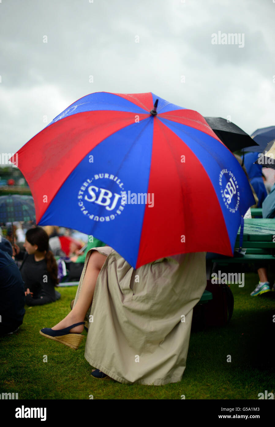 Tennisfans schützen sich vor dem Regen, da das Spiel am achten Tag der Wimbledon Championships 2012 im All England Lawn Tennis Club in Wimbledon gestoppt wird. Stockfoto