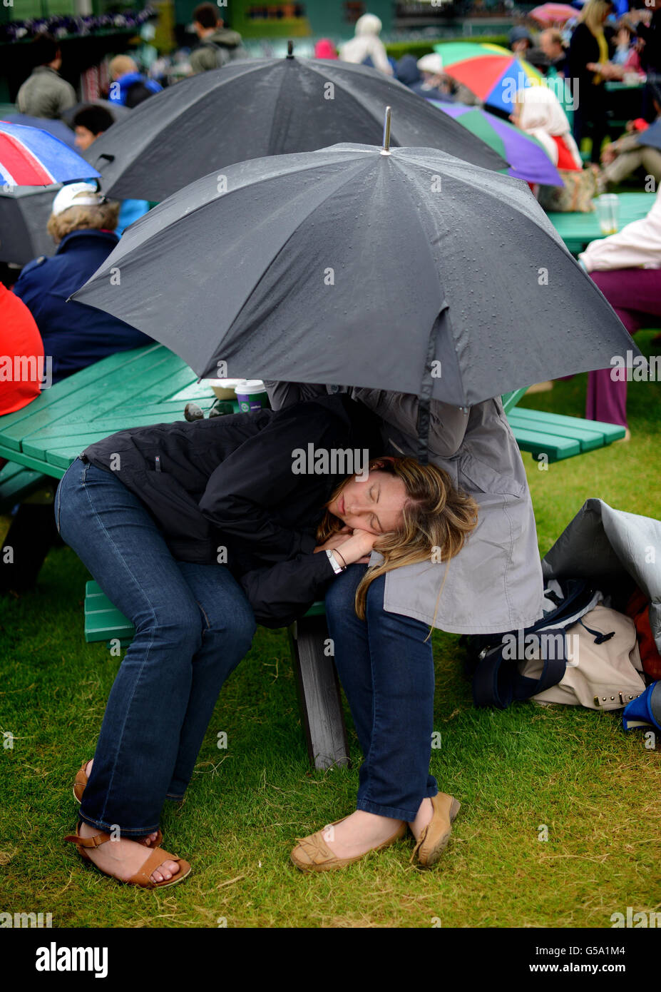 Tennisfans schützen sich vor dem Regen, während sie am achten Tag der Wimbledon Championships 2012 im All England Lawn Tennis Club in Wimbledon auf den Neustart warten. Stockfoto