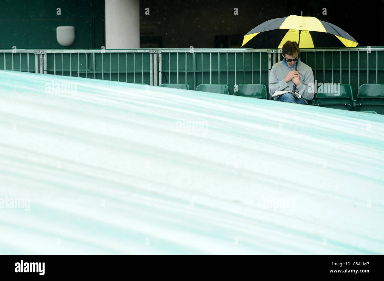 Ein Tennisfan schützt vor Regen, da das Spiel am achten Tag der Wimbledon Championships 2012 im All England Lawn Tennis Club in Wimbledon gestoppt wird. Stockfoto
