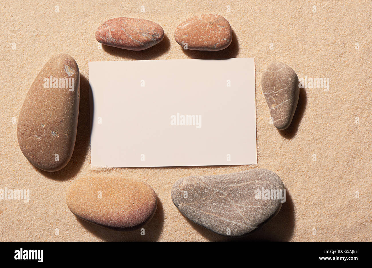Rechteckiger Rahmen sechs kleine und große Meer Steine mit leeren weißen Visitenkarte auf Sand. Sommer Strand Hintergrund Stockfoto