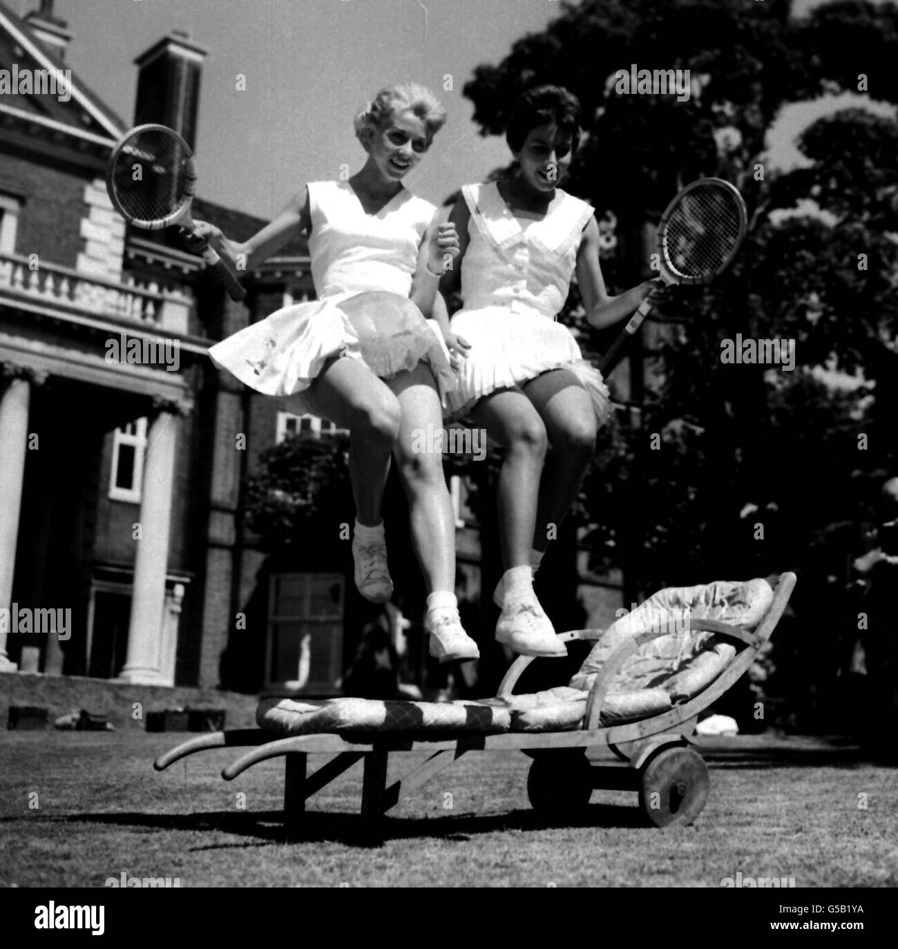 Röcke fliegen, während die Italienerin Lea Pericoli (links) und die Brasilianerin Maria Xeno bei Lady Crosfields jährlichen Tennisspielen, die in ihrem Haus in Highgate, London, stattfinden, einen Stuhl springen. Die Partei, die Wimbledon als Vorhangsparty einführt, dient der Nächstenliebe. Stockfoto