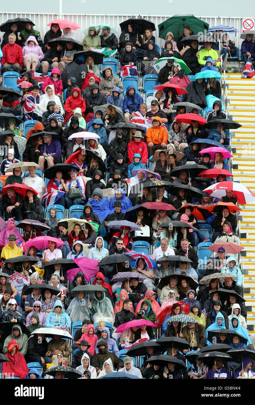 Die Zuschauer schützen sich vor dem Regen, während sie den 2. Qualifikator des Reitsportes Jumping Individual und die Eröffnungsrunde des Team Competition im Greenwich Park, London, während des neunten Tages der Olympischen Spiele 2012 in London beobachten. Stockfoto