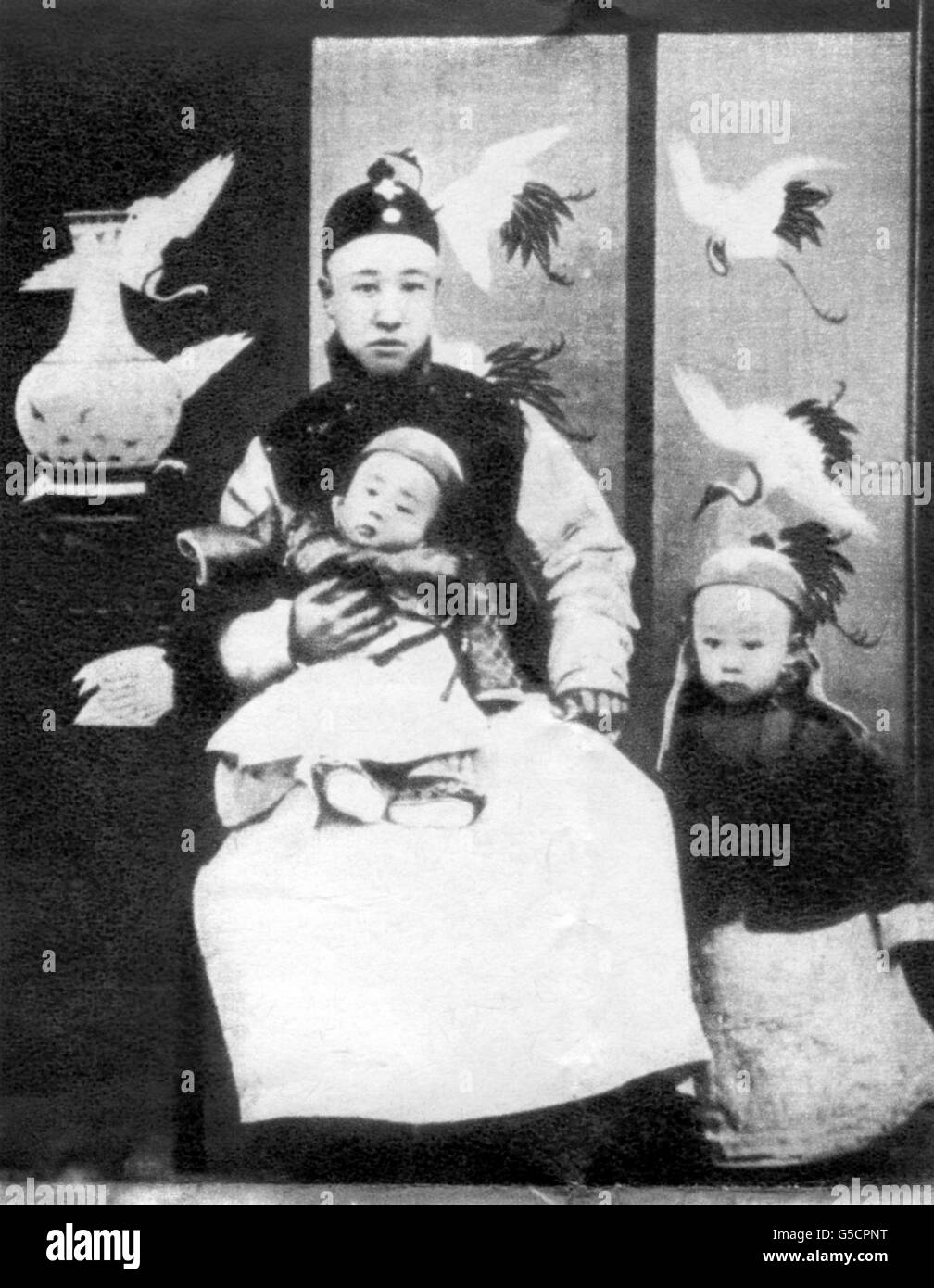 Der dreijährige Aisin-Gioro Puyi, der Xuantong-Kaiser von China, der 1912 abdankte und noch immer unter dem Namen Henry Puyi in Peking lebt. Er wird hier auf dem Knie seines Vaters, des Regenten, Prinz Zaifeng Chun, gesehen. Sein jüngerer Bruder Prinz Pujie steht neben ihnen. Stockfoto