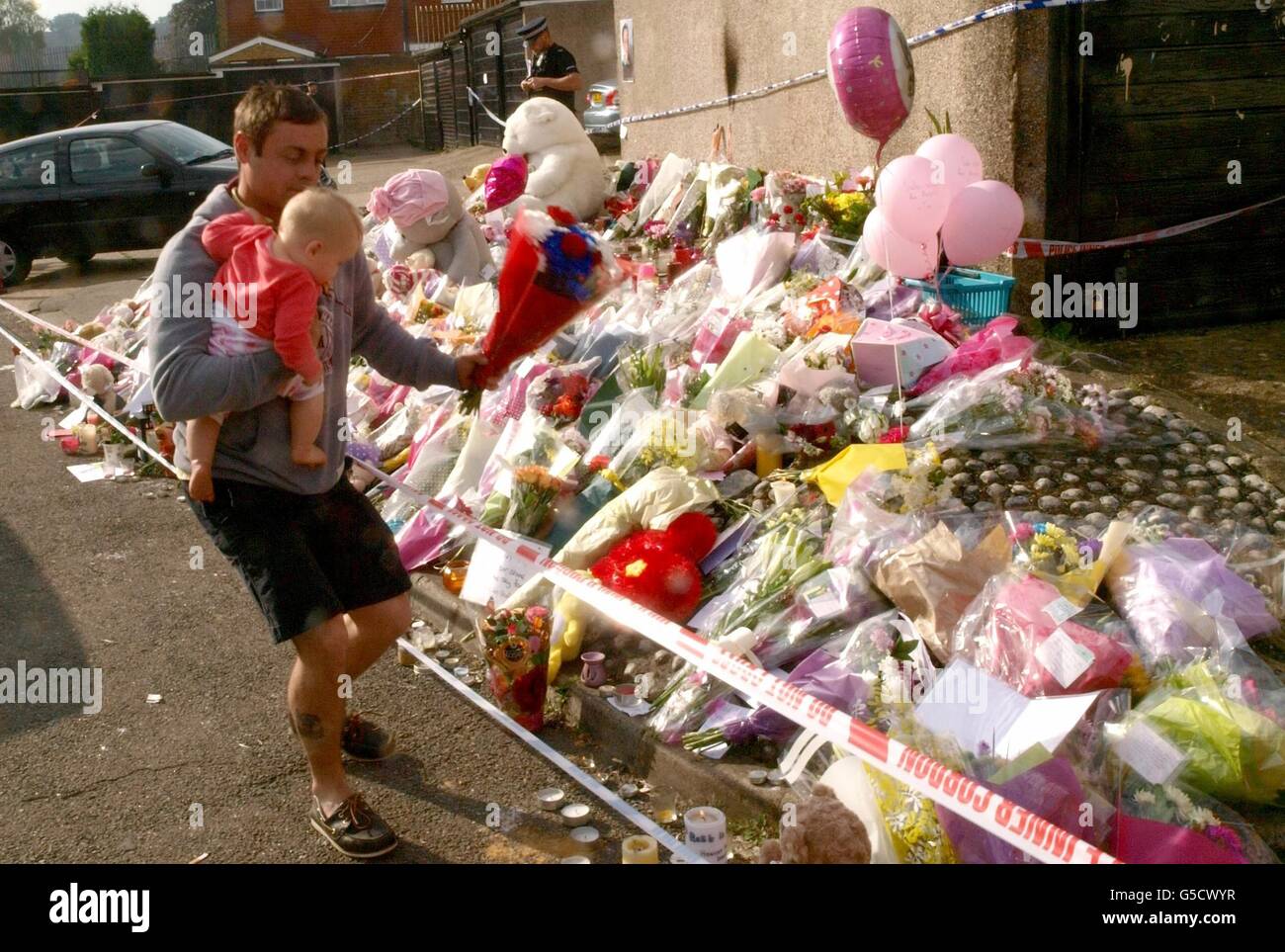 Ein Vater, der seinen Sohn in den Armen hält, legt einen Strauß auf den Schrein für Tia Sharp in der Nähe des Hauses ihrer Großmutter in New Addington, Croydon. Stockfoto