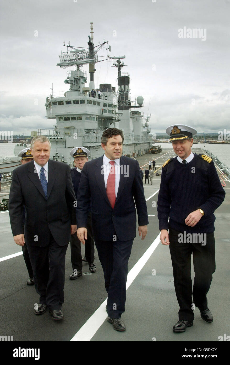 Kanzler Gordon Brown (Mitte) und Bundeswehrminister Adam Ingram (links) starten nach einer Führung durch HMS Ark Royal durch Kommandant David Snelson, da es vor Anker neben der Forth Road und der Rail Bridges liegt. Stockfoto