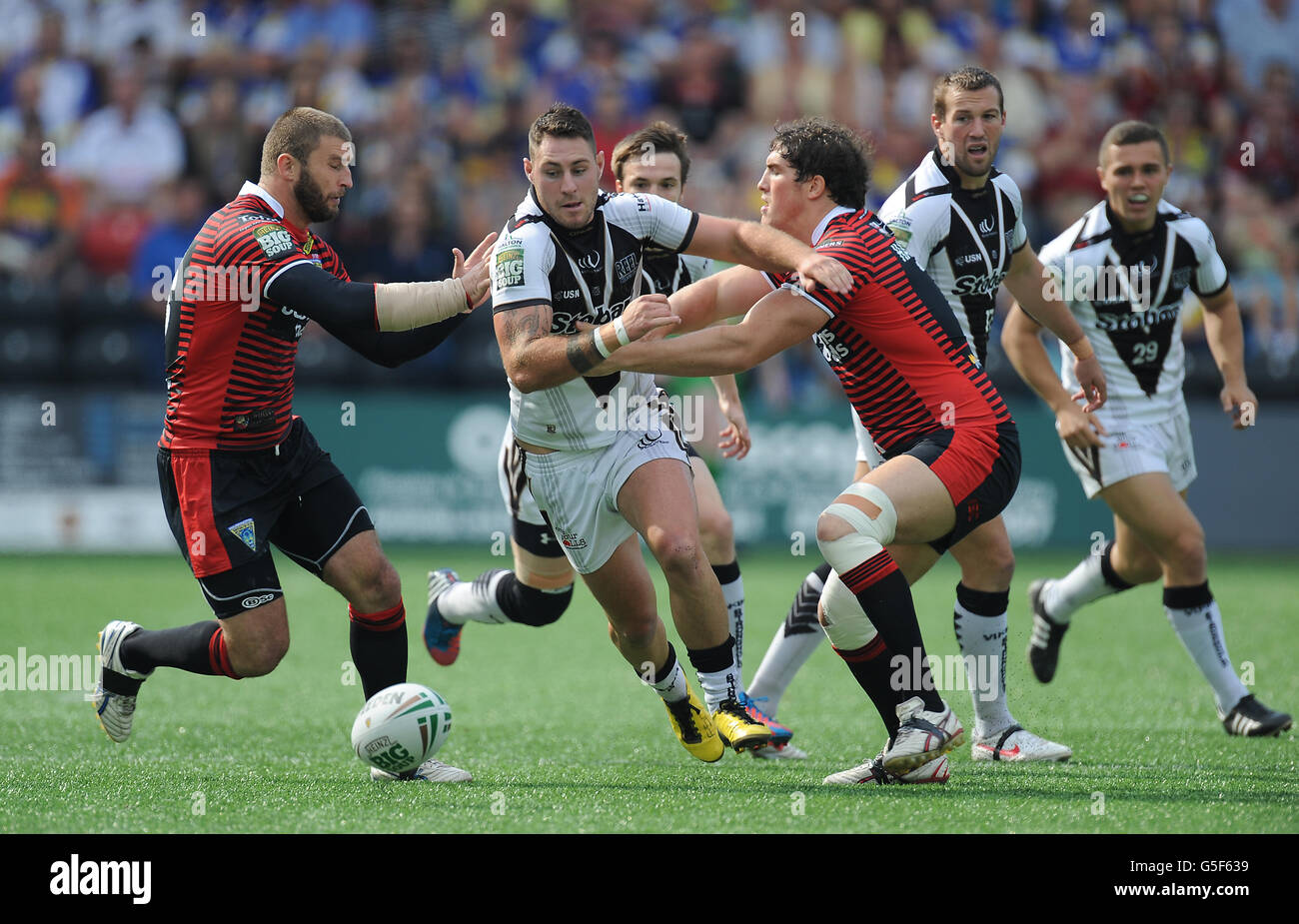 Der Kurt Haggerty von Widnes Vikings verläuft zwischen Paul Wood von Warrington Wolves und Ben Harrison Stockfoto