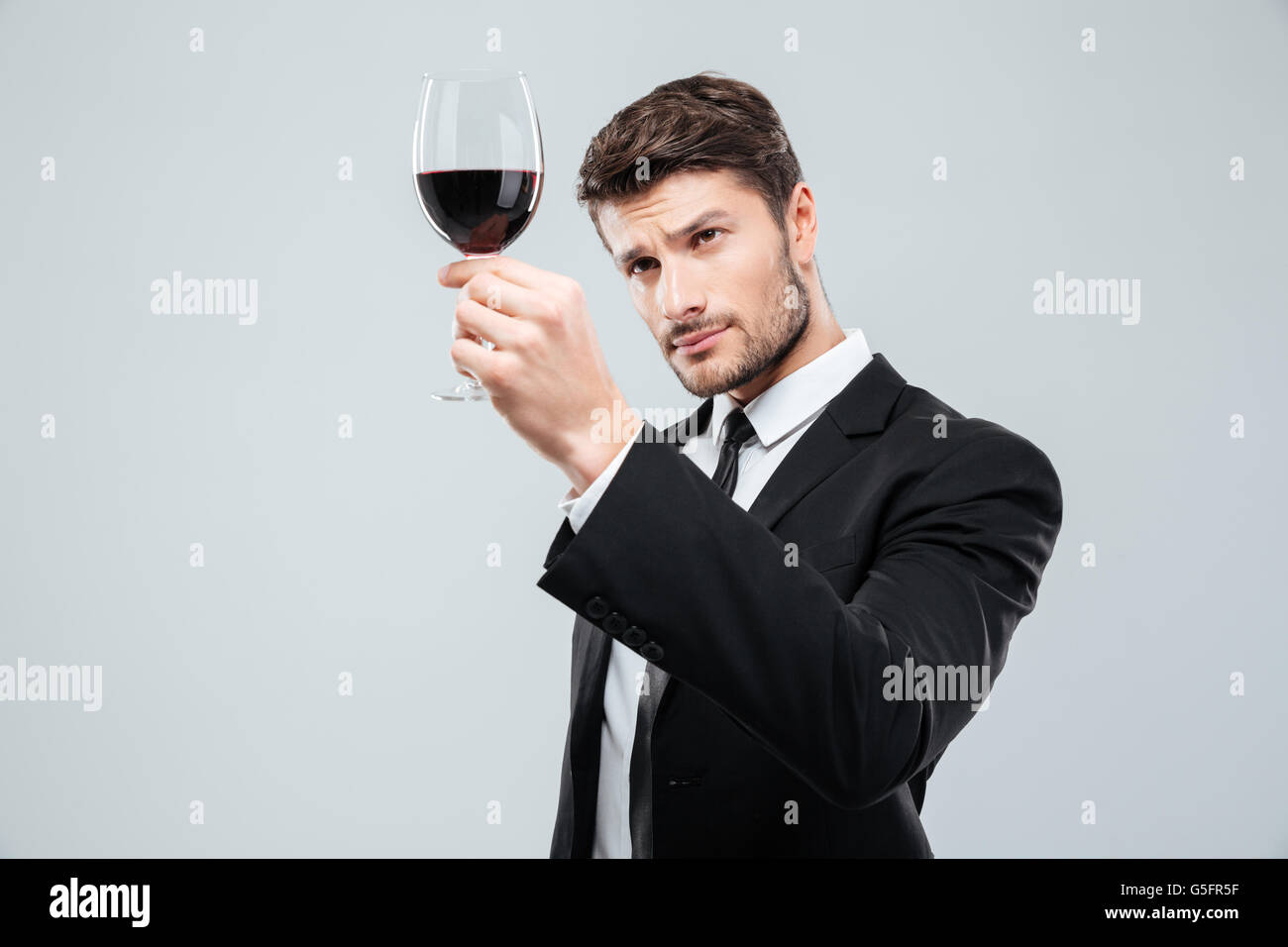 Konzentriert junger Mann Sommelier Weinproben und Blick auf Rotwein im Glas auf weißem Hintergrund Stockfoto