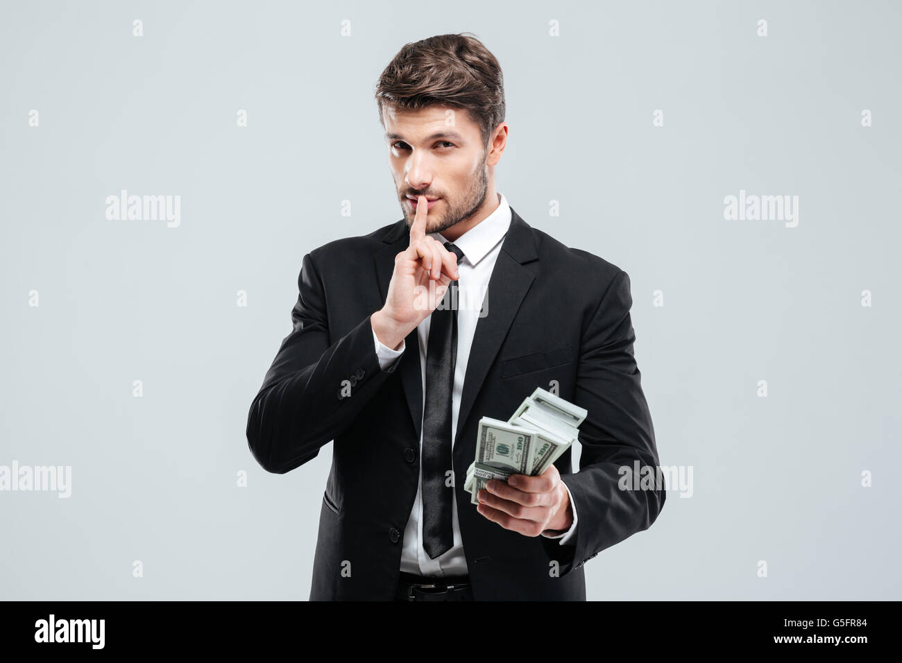 Hübscher junger Geschäftsmann Betrieb Geld und zeigt Stille unterzeichnen auf weißem Hintergrund Stockfoto