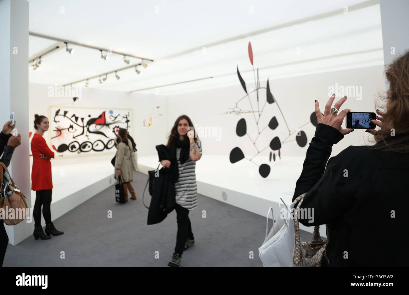 Die Besucher sehen einen Raum mit einem Gemälde von Joan Miro (links, der schmerzhafte Marsch unter der Führung des Flamboyant Bird of the Desert, 1968) und einer Skulptur von Alexander Calder (Triumphant Red, 1959-63) auf der Frieze Masters Kunstmesse im Regents Park im Zentrum von London. Stockfoto