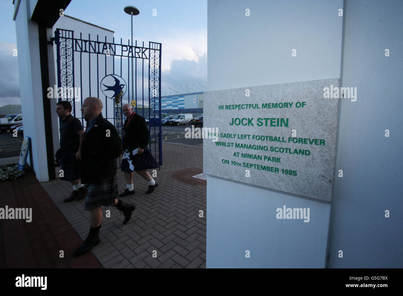 Schottland-Fans Gary McNamara, Jim Cooper, Bruce Giles laufen an den alten Ninian Park Gates vorbei, mit der Gedenktafel an den ehemaligen schottischen Manager Jock Stein vor dem FIFA-WM-Qualifikationsspiel 2014 im Cardiff City Stadium, Cardiff. Stockfoto