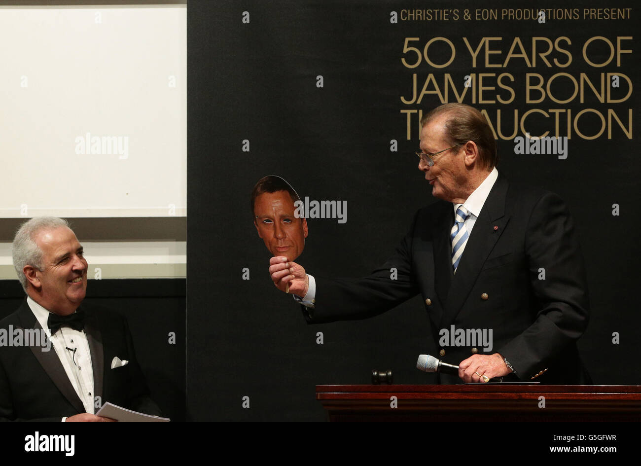 Sir Roger Moore hält eine Maske des aktuellen James-Bond-Schauspielers Daniel Craig mit dem Auktionator Hugh Edmeades bei Christie's 50 Years of James Bond Sale, mit Erinnerungsstücken, die von der Bond-Besetzung gespendet wurden, in Christie's in South Kensington, London. DRÜCKEN Sie VERBANDSFOTO. Bilddatum: Freitag, 5. Oktober 2012. Siehe PA Story SALE Bond. Bildnachweis sollte lauten: Yui Mok/PA Wire Stockfoto