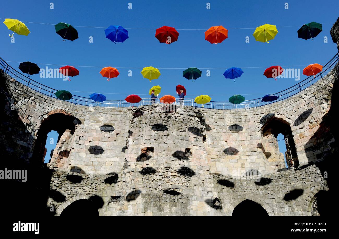 Louise Wyatt und Steve Parker von English Heritage stehen in einer neuen Kunstinstallation namens „Umbrella Sky“ im Clifford's Tower, York. Die Installation besteht aus 45 farbigen Regenschirmen, die in den historischen Mauern aufgehängt sind, und ist ein unbeschwerter Blick auf das schlechte Wetter der Stadt. Stockfoto