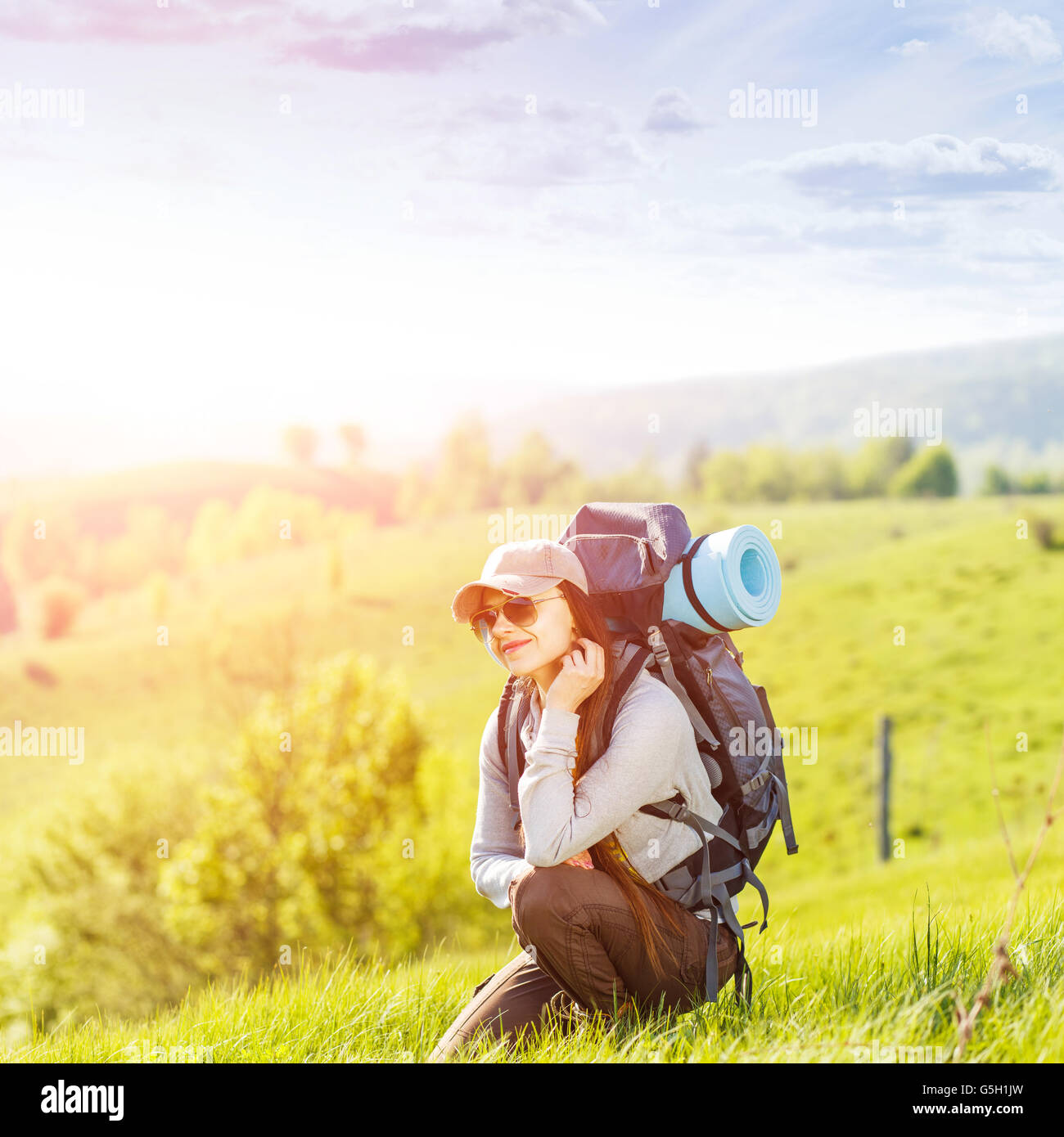 Junge glückliche Frau mit Rucksack auf grünem Hügel im Sonnenaufgang Balken ruht. Schöne Reisen Backpacker Hintergrund mit Kopie spac Stockfoto