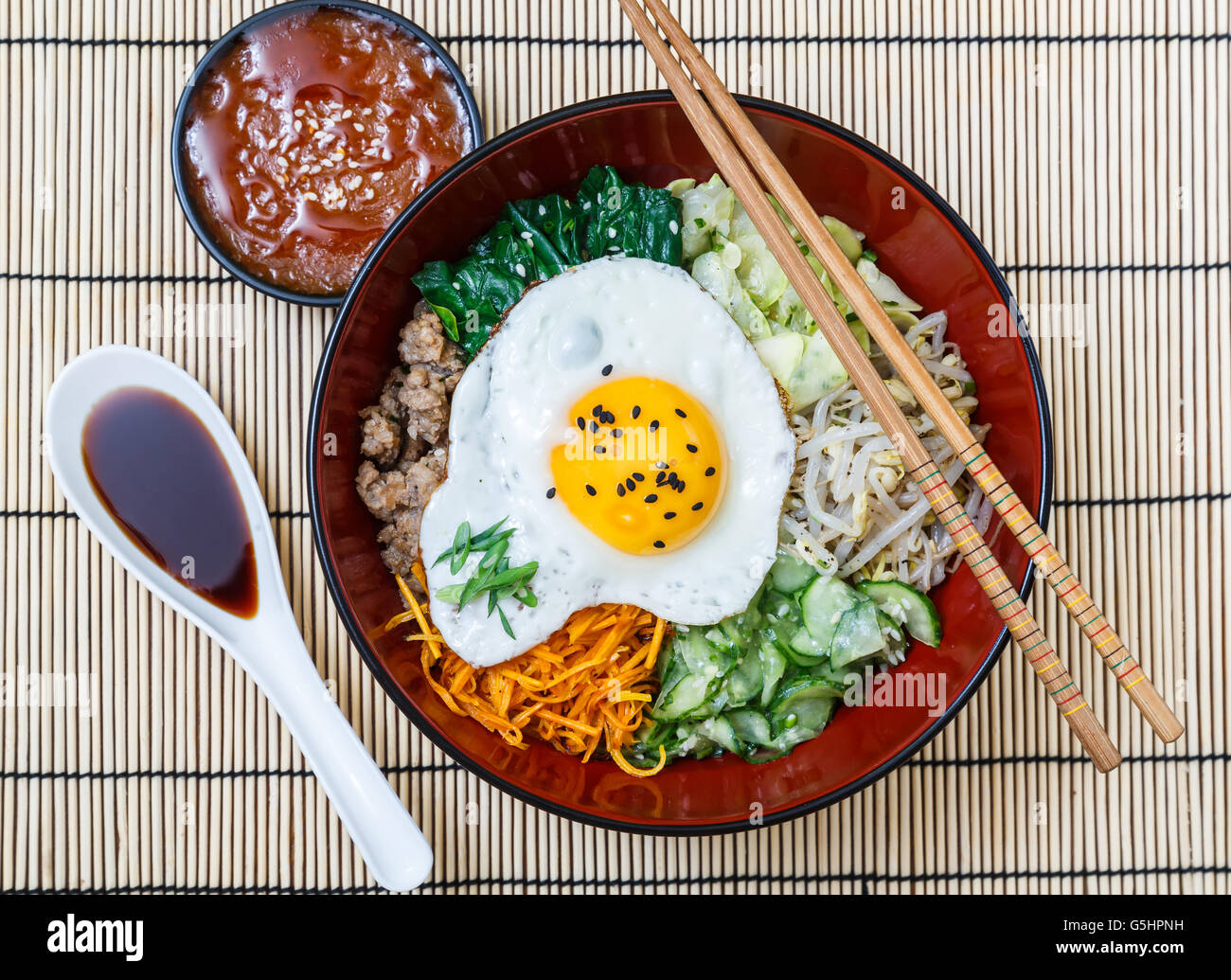 in einer Schüssel mit Soßen auf Bambusmatte, koreanische Gericht Bibimbap. Stockfoto in einer Schüssel mit Soßen auf Bambusmatte, koreanische Gericht Bibimbap. Stockfoto