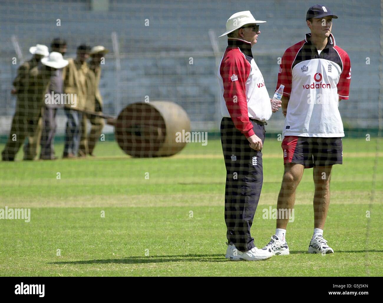 Groundstaff schiebt eine schwere Rolle, um den Platz vorzubereiten, während England-Trainer Duncan Fletcher (links) und England-Physiologe Nigel Stockill Netzübungen in Mumbai, Indien, beobachten. Stockfoto