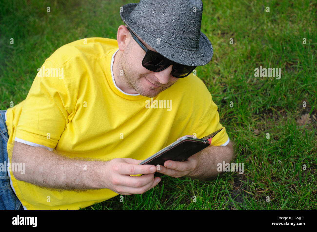 kluger junger Mann in ein gelbes T-shirt mit dem Telefon auf dem Rasen Stockfoto