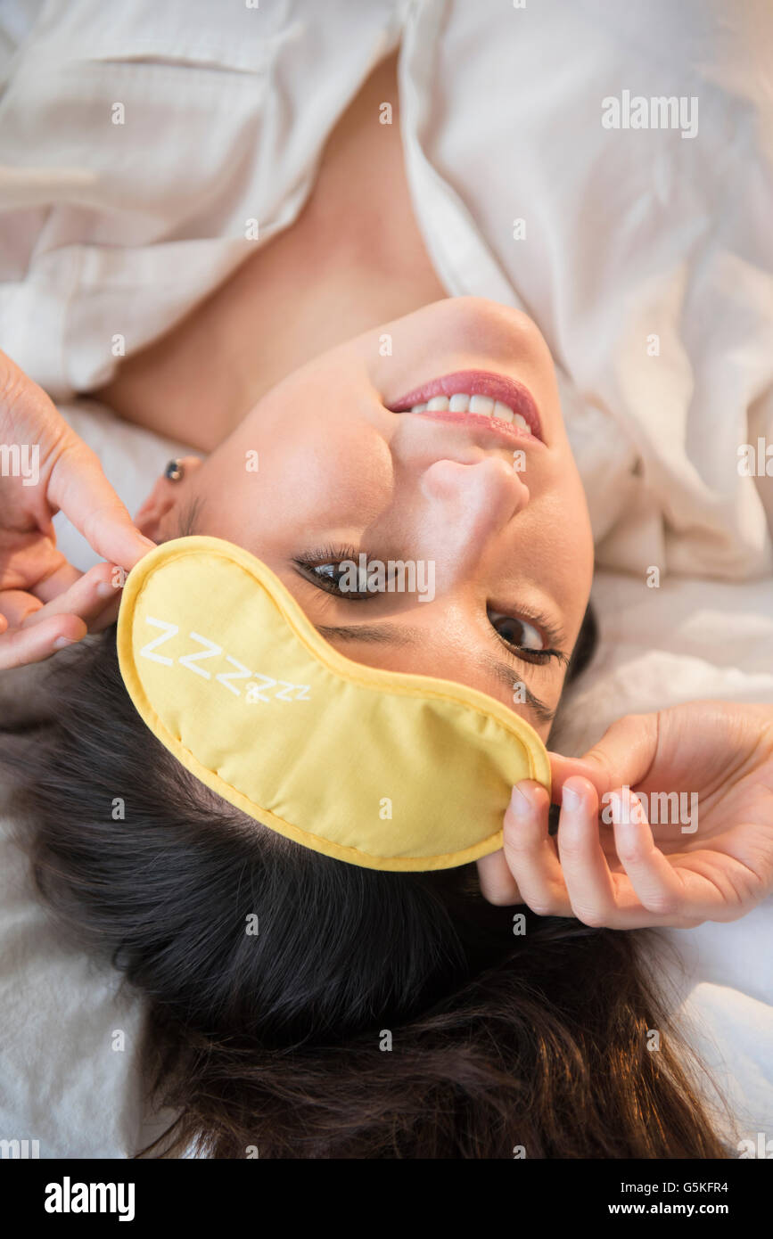 Lächelnde Frau tragen Augenmaske auf Bett Stockfoto