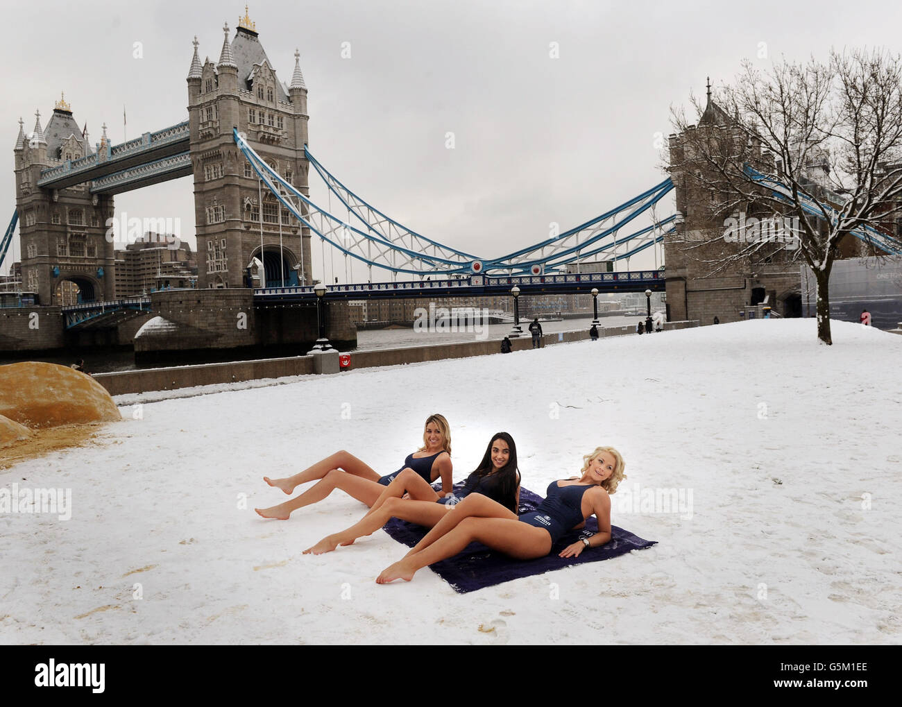 Drei Modelle liegen auf Strandtüchern neben der Tower Bridge, während Hilton Hotels & Resorts einen Pop-up-Strand an der Themse, London, an dem Tag schaffen, der von vielen als der deprimierendste Tag des Jahres angesehen wird. Stockfoto