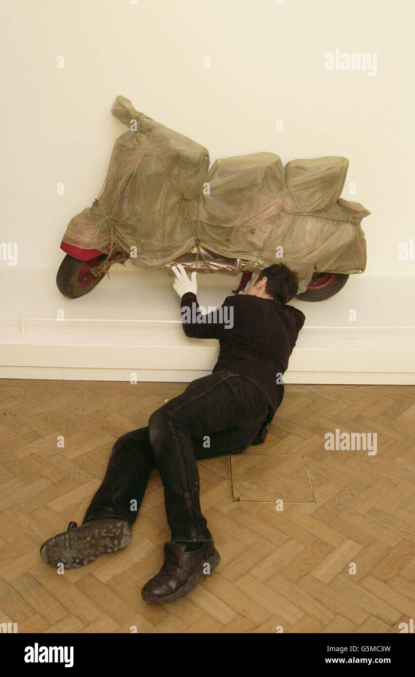 John Potter, ein Kunsthandler aus London, unterm Inneren der Royal Academy of Arts, London, ein lebensgroßes Vespa-Motorrad, das in Polythene gehüllt ist, ein Kunstwerk des international gefeierten bulgarischen Künstlers Christo. Das Stück ist Teil der Ausstellung "Paris : Capital of the Arts 1900-1968", die für die Öffentlichkeit zugänglich sein wird und in der Akademie verbleiben wird, bevor sie ins Guggenheim Museum in Bilbao umziehen. Stockfoto