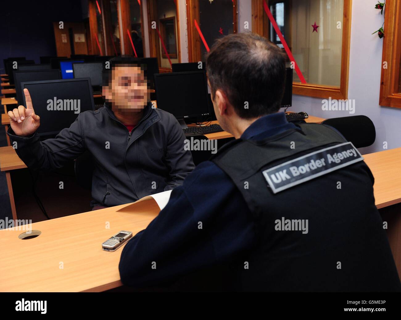 GESICHT VERPIXELT VOM PA-BILDTISCH EIN Offizier der britischen Grenzbehörde spricht mit einem Studenten während eines Überfalls auf mutmaßliche Einwanderungsdelikte am Leeds Professional College, Leeds. Stockfoto