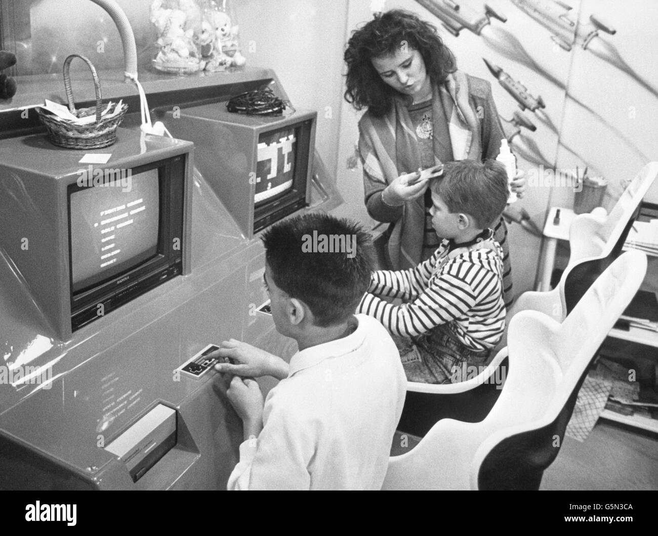 In einem Friseursalon in Colmer im Elsass in Ostfrankreich kann Jean-Jacques Henry die Kinder nicht fernhalten, da er Videocomputerspiele installiert hat, um sie bei einem Haarschnitt zu unterhalten. Stockfoto