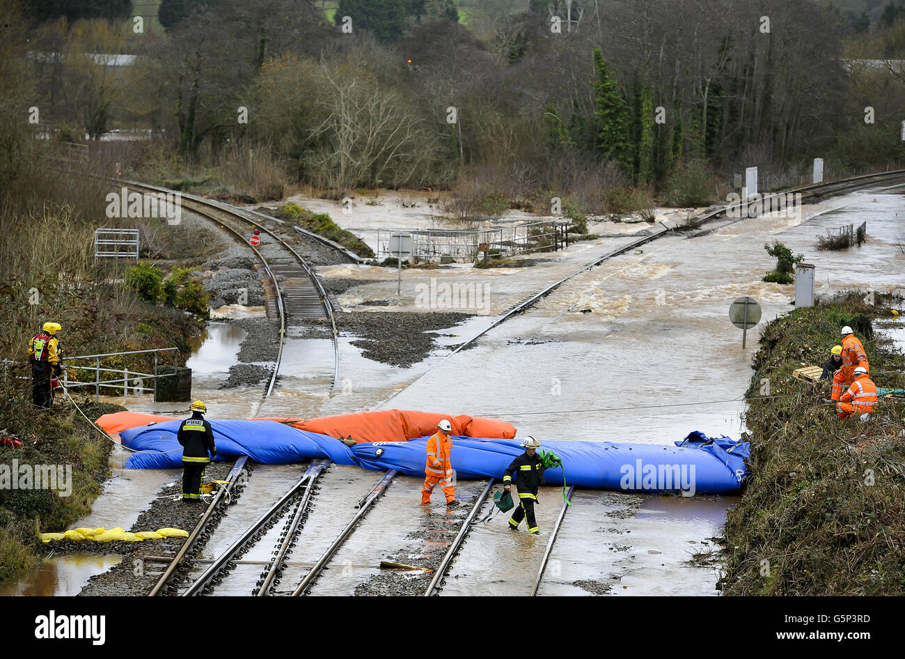 Eisenbahningenieure und Feuerwehr- und Rettungsdienstmitarbeiter überwachen die aufblasbaren Staudämme auf der Eisenbahnlinie an der Cowley Bridge bei Exeter, Devon, während sie versuchen, den Wasserfluss dort einzudämmen, wo die Strecke überflutet wurde und strukturelle Schäden verursacht hat und die Linien über Weihnachten schließen. Stockfoto