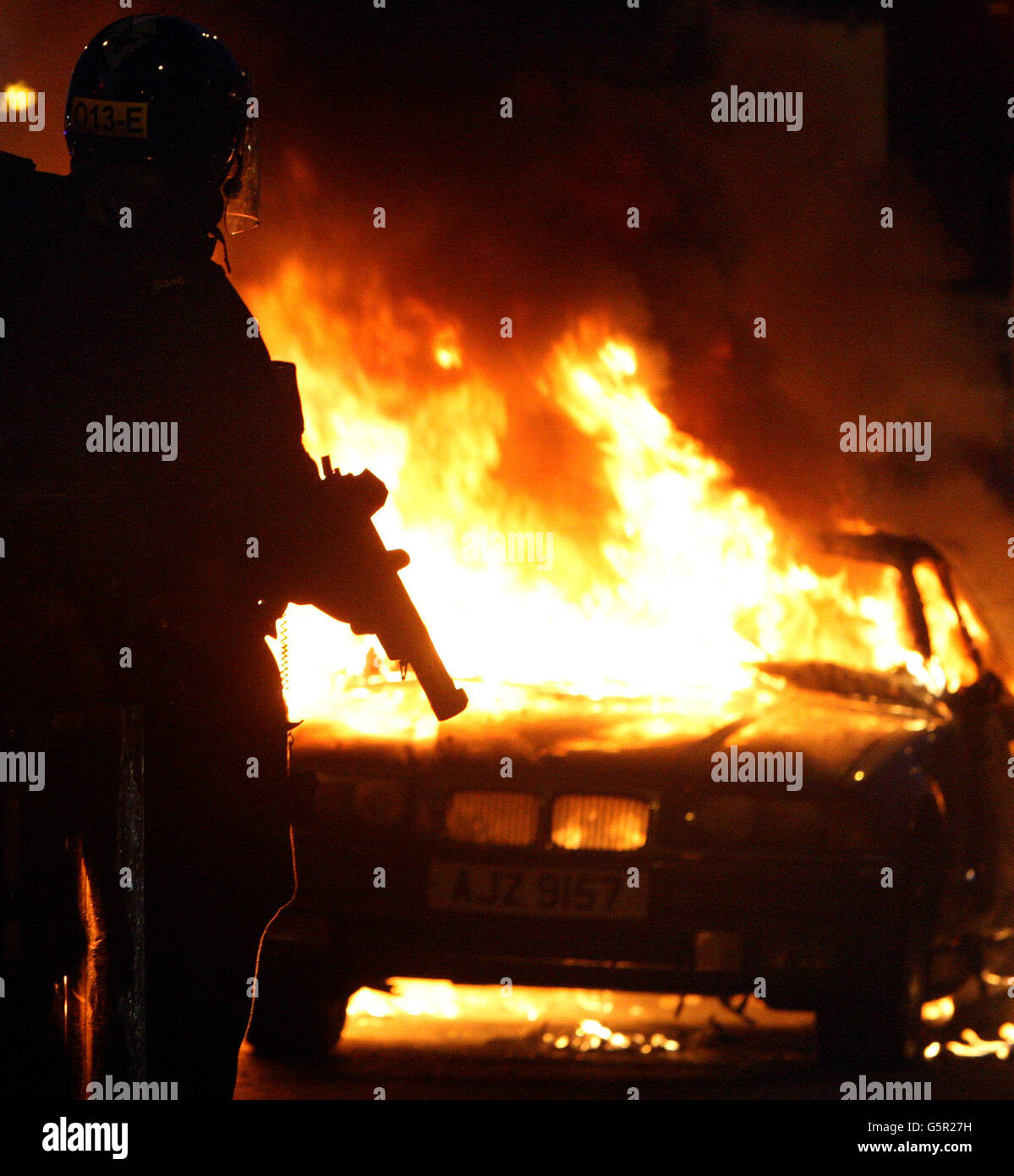 Die Bereitschaftspolizei steht neben einem ausgebrannten Auto, nachdem loyalistische Demonstranten Polizeilinien angegriffen hatten, im Osten von Belfast. Stockfoto