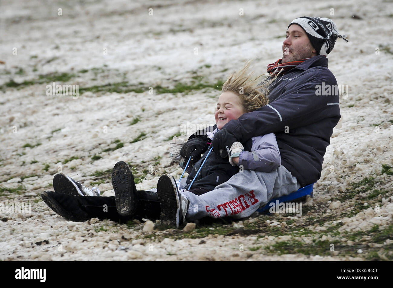 Schlittenfahrer haben immer noch Spaß, wie der Schnee wird lückenhaft und langsam verwandelt sich in Schlamm auf dem Hügel im Arnos Park in Brislington, Bristol. Stockfoto