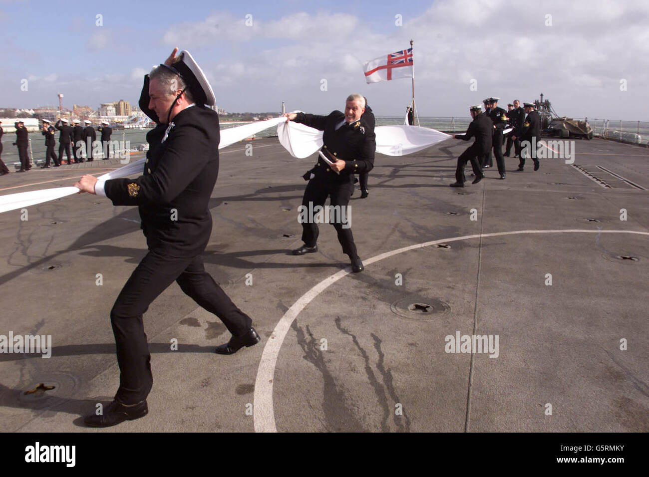 Segler auf der HMS Fearless hängen an ihren Hüten und einer 158 Meter langen Flagge, als sie zum letzten Mal nach Portsmouth zurückkehren.Montag, 18. März 2002. Die auszahlende Wimpel wird geflogen, wenn ein Schiff aus dem Dienst genommen wird, leider schwere Orkanstärke 9 Winde verursacht logistische Probleme. *...das Sturmschiff ist das längste Schiff der aktiven Kriegsschiffe der Marine und das einzige verbliebene dampfgetriebene Schiff. Sie soll nach einer illustren 36-jährigen Karriere, die die Rettung von James Bond in "der Spion, der mich liebte" beinhaltete, außer Dienst gestellt werden. Der Falklandkrieg von 1982 rettete Fearless vor einem früheren Versuch Stockfoto