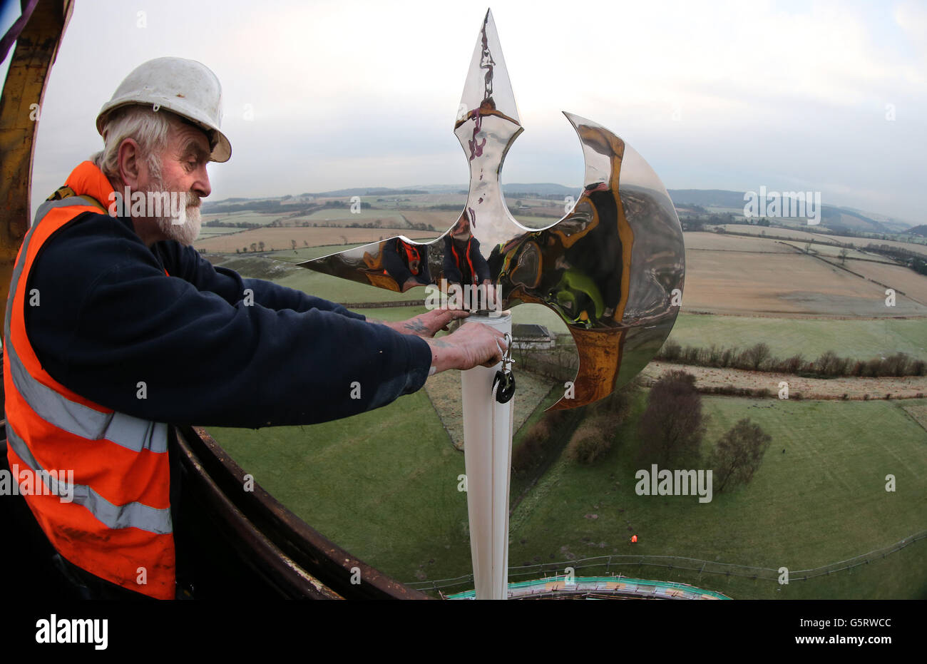Der Fahnenmast-Ingenieur Brian Whitfield stellt eine neue Windfahne an der Schlachtaxe von Robert the Bruce ein, nachdem er sie nach der Reparatur des Fahnenmastes rechtzeitig zum 700. Jahrestag der Schlacht von Bannockburn im nächsten Jahr am Bannockburn-Fahnenmast in Stirlingshire installiert hatte. Stockfoto