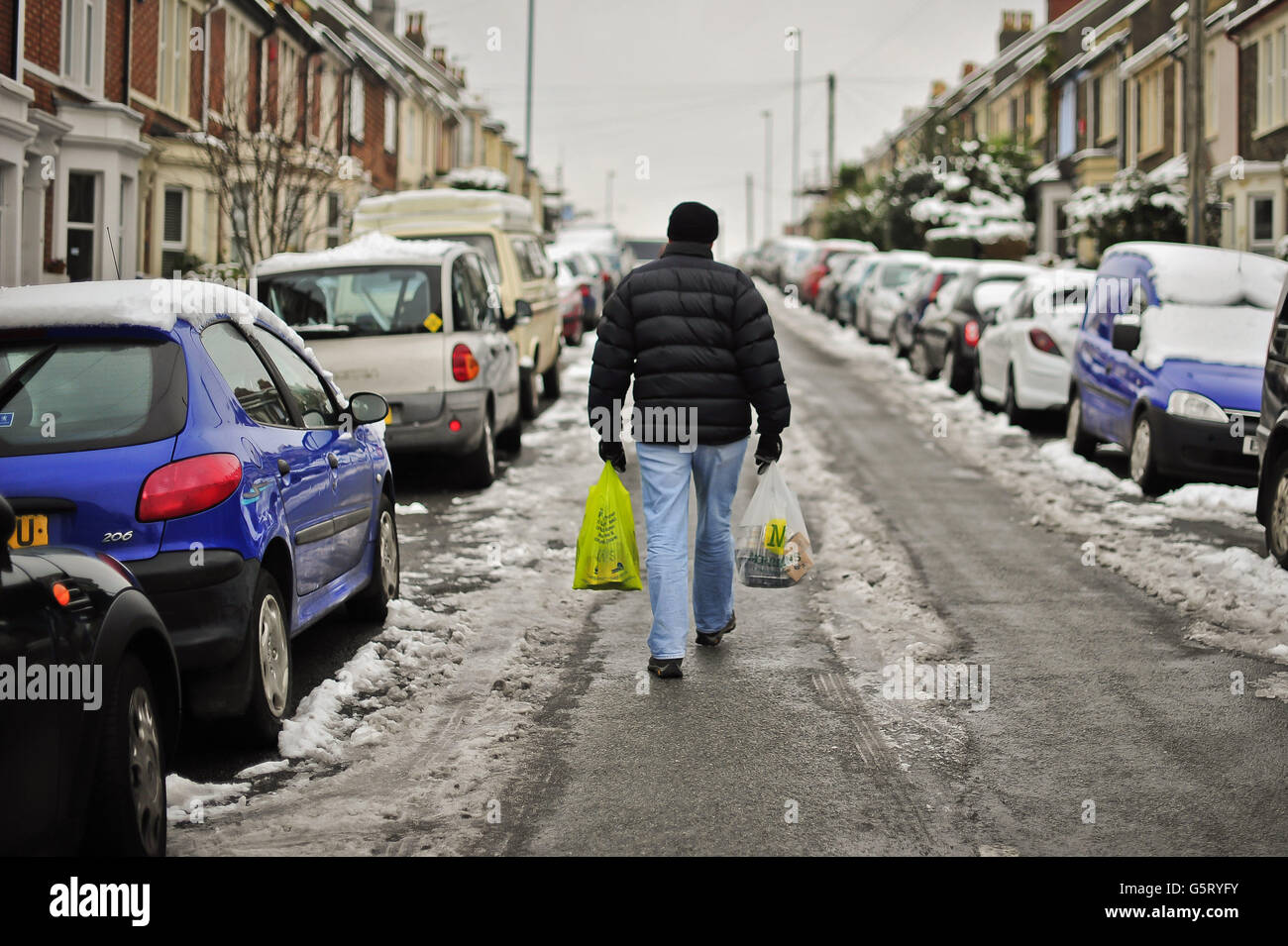 Ein Mann geht in der Straße mit Einkaufstaschen, da die meisten Wege rund um Bristol sind mit kompakten Schnee und Eis bedeckt. Stockfoto