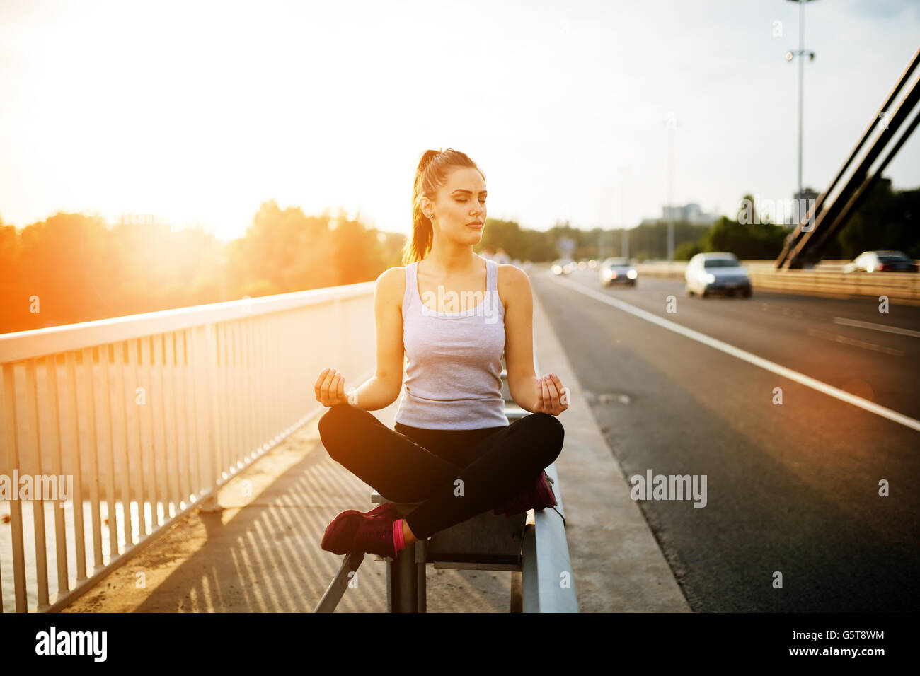 Schöne Frau im Lotussitz auf Brücke neben Autos - Konzept Stockfoto