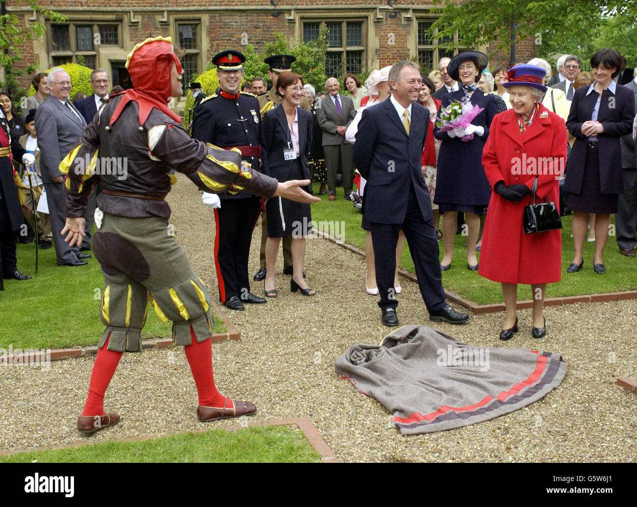 Königin Elizabeth II. Wird eingeladen, während ihres Golden Jubilee-Besuches in East London auf einem Kap zu treten, das ihr ein elisabethischer Narr alias Peet Cooper im Eastbury Manor House zu Füßen wirft. Stockfoto