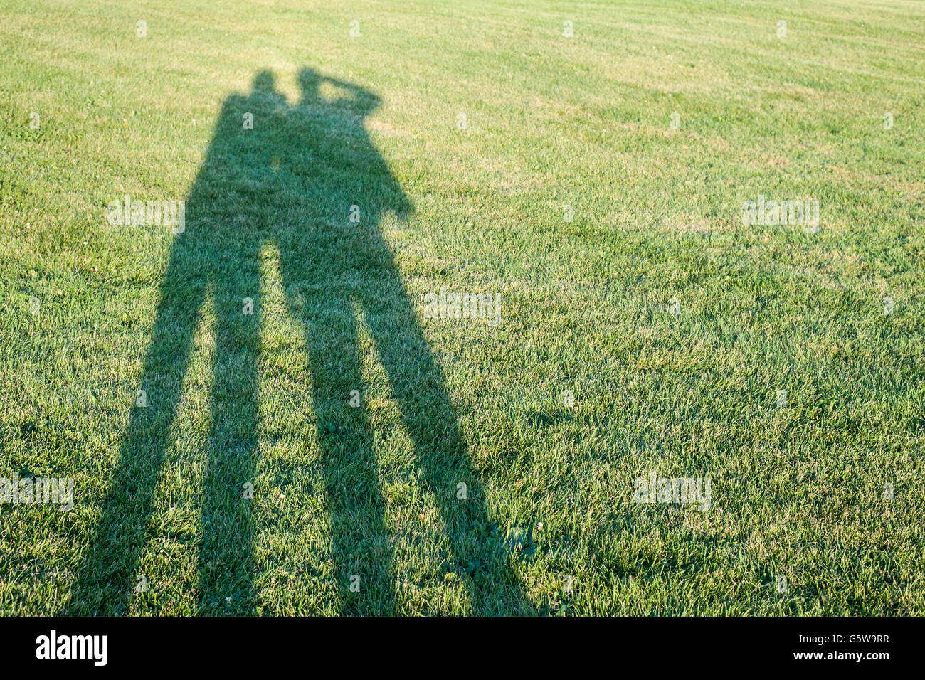 Lange Schatten zweier Menschen fotografieren stehen auf Rasen mit Textfreiraum Stockfoto