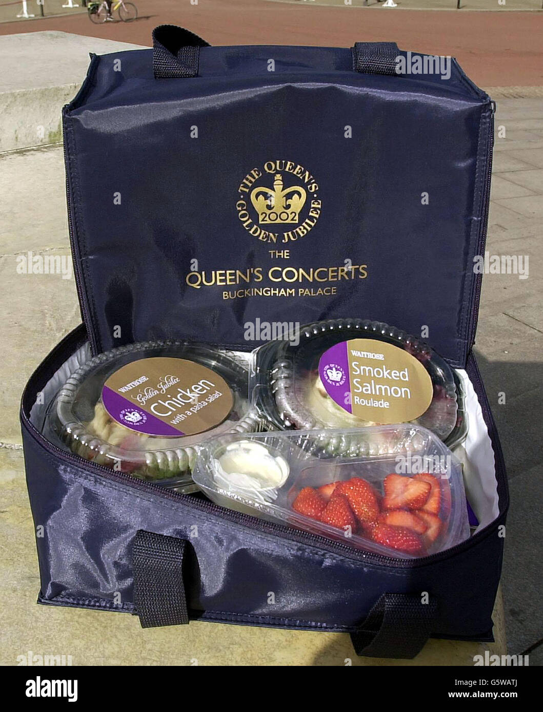 Einer der 24,000 Picknickkörbe, die an die Konzertbesucher des Golden Jubilee im Buckingham Palace verteilt werden und vor dem Palast ausgestellt werden. Die kostenlose Souvenir-Kühltasche ist mit geräucherter Lachsroulade, Jubilee-Huhn und Nudelsalat, Erdbeeren und Sahne verpackt. * .... eine halbe Flasche Lanson Champagner, Cadburys Schokolade, Herzogtum Originals Haferkuchen mit freundlicher Genehmigung des Prinzen von Wales und Mineralwasser. Zusätzlich enthält jede navy cool Tasche eine Sektflöte aus Kunststoff, ein Besteckpaket mit Serviette und einen Regenponcho in passendem Marineblau mit einem Queen's Concerts Logo. 07/08/02 : einer von Stockfoto