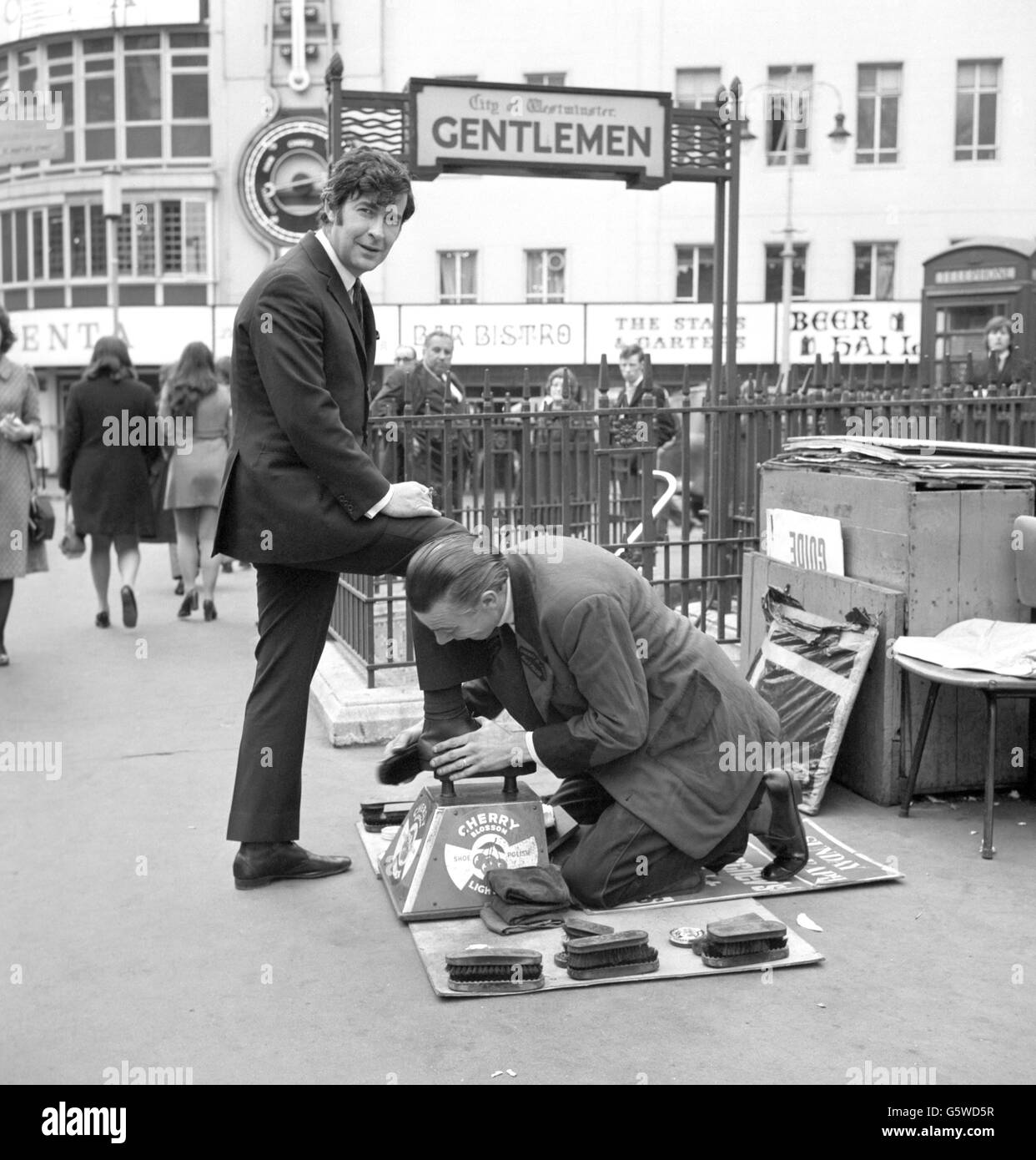 Der in Dublin geborene Komiker Dave Allen machte einen Zwischenstopp auf dem Leicester Square in London, um einen Schuh zu glänzen. Er war auf dem Weg zum nahe gelegenen Talk of the Town Restaurant, wo er für eine einmonatige Saison für Bernard Delfont eröffnet. Dave kam 1967 zum ersten Mal in das Restaurant. Stockfoto