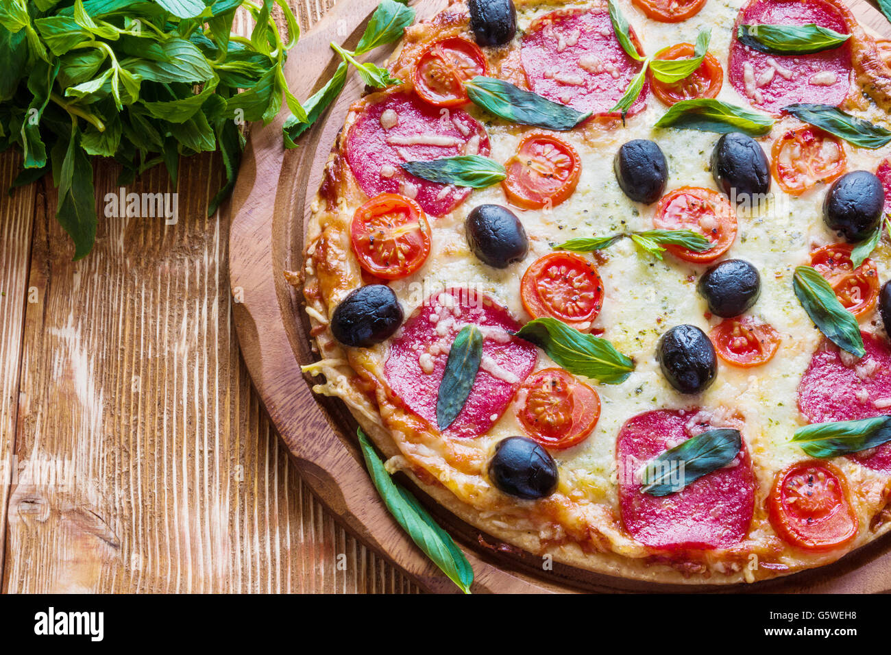 Pizza mit Salami, schwarzen Oliven und Tomaten auf dem Holztisch. Stockfoto