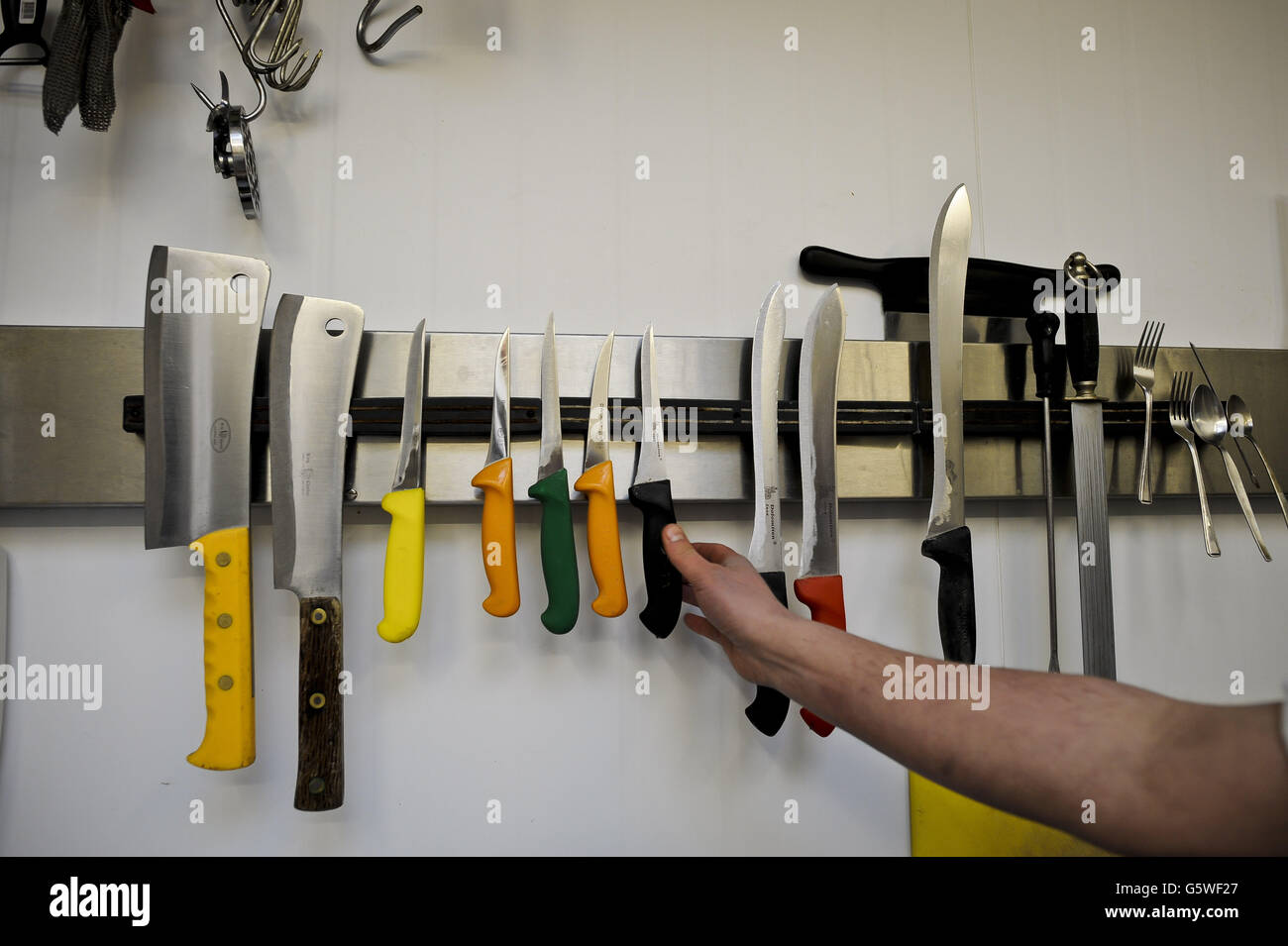 Metzger erhöhen den Handel. Eine Hand reicht, um ein Metzgermesser aus dem Magnetständer im Sheeprove Organic Farm Shop in Bristol zu greifen. Stockfoto