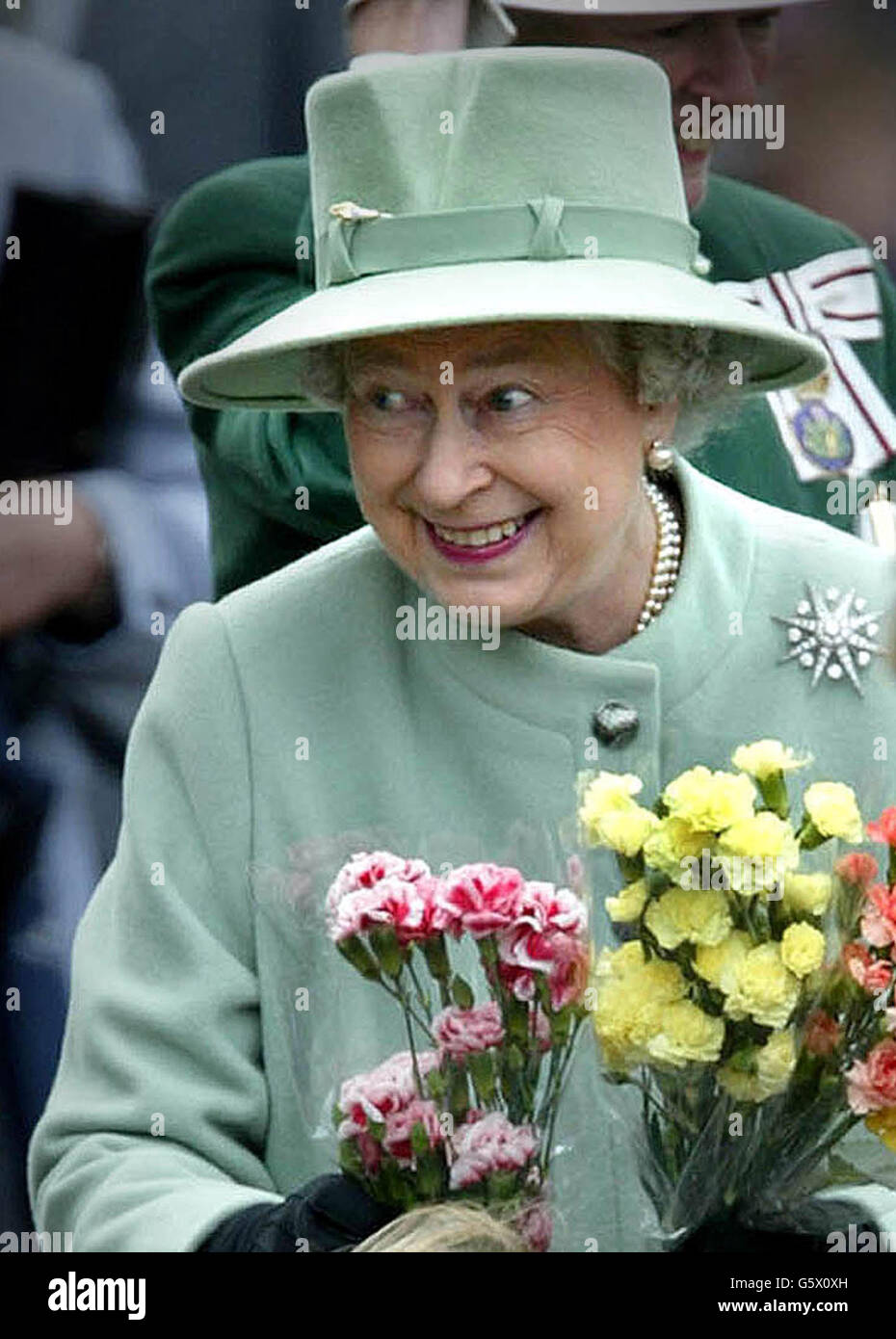 Die britische Königin Elizabeth lächelt, als sie bei ihrem Spaziergang auf dem Melrose Market Square in den Scottish Borders von Kindern mit Blumen überreicht wird. Stockfoto