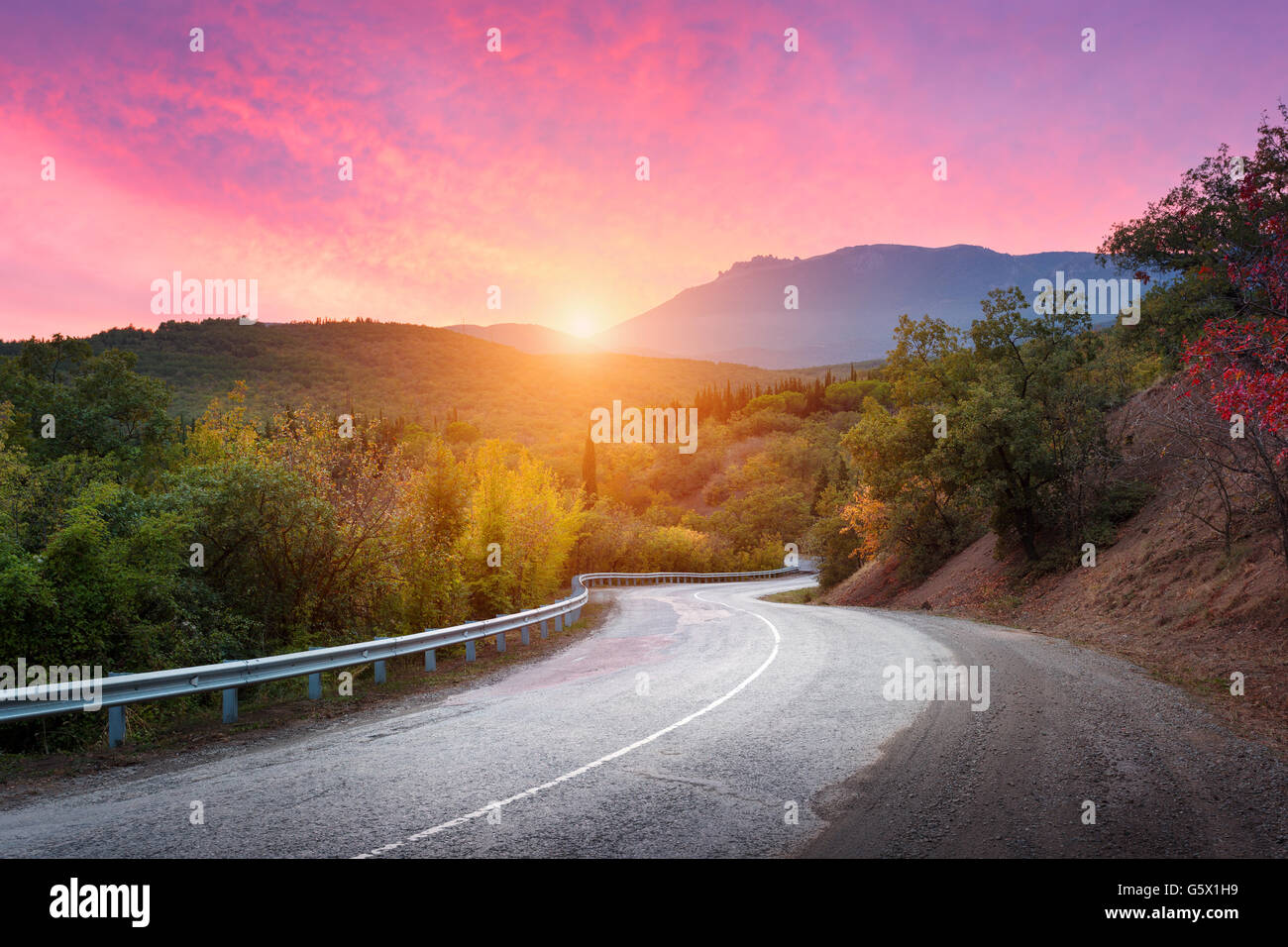 Bergstraße vorbei durch den Wald mit dramatischen bunten Himmel und rote Wolken am farbenprächtigen Sonnenuntergang im Sommer. Berg-si Stockfoto