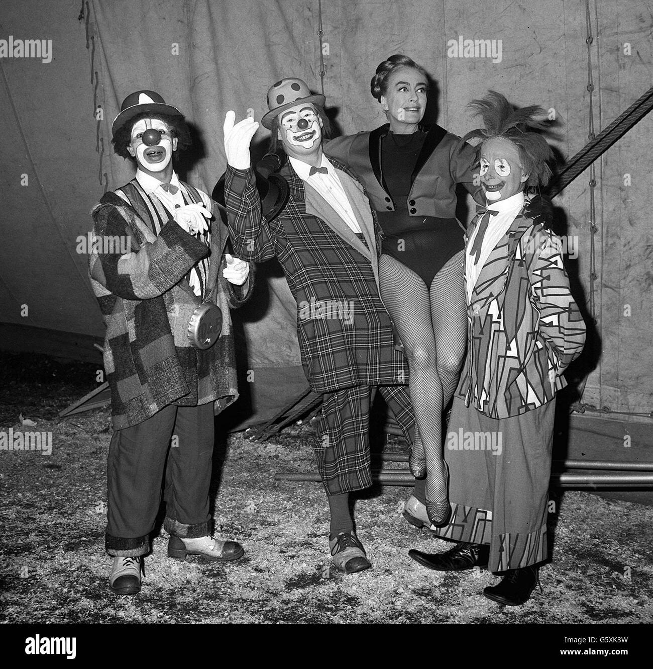 In einem Kostüm mit Netzstrumpfhose erhält die Hollywood-Schauspielerin Joan Crawford die Unterstützung von einem oder zwei der Clowns im Zirkus von Billy Smart, als sie als Ringmeisterin für eine Wohltätigkeitsveranstaltung unter dem großen Dach von Blackheath tätig war. Stockfoto