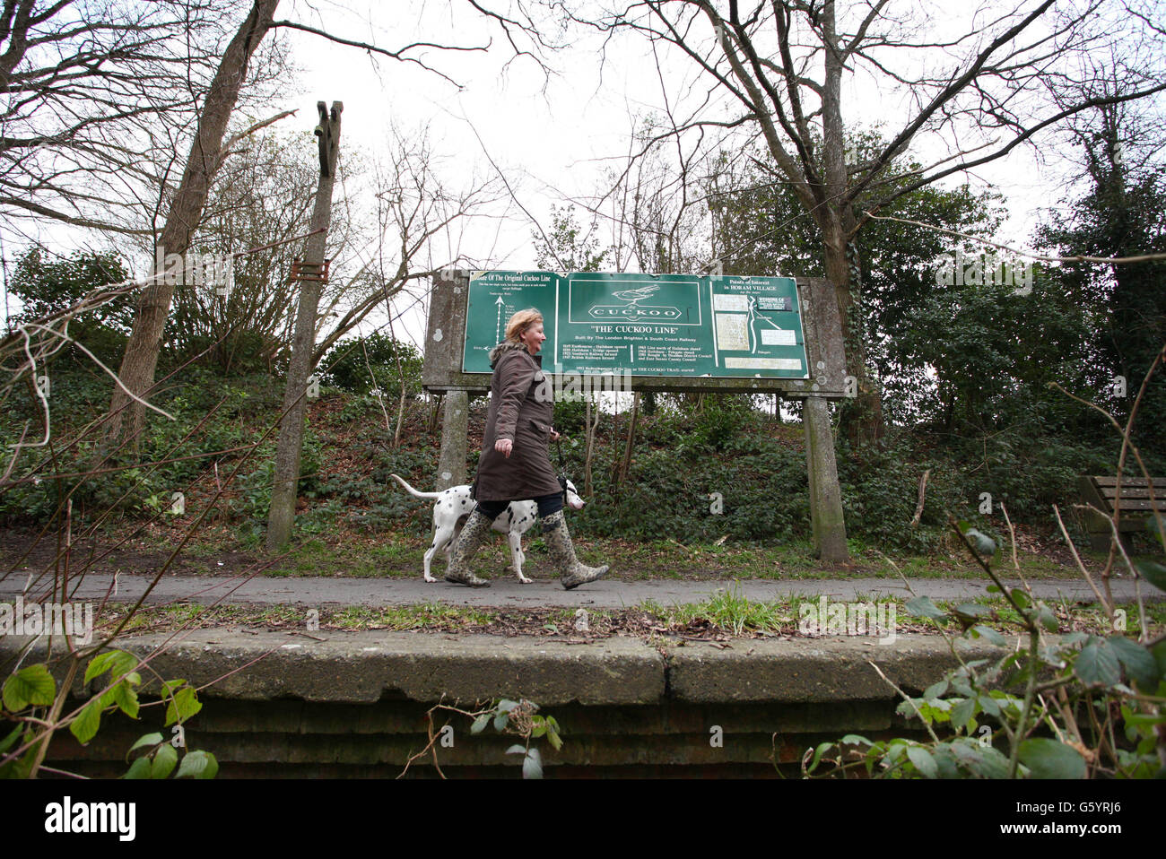 Eine Dame führt ihren Hund entlang der Überreste des Bahnsteigs am ehemaligen Bahnhof der Kuckucklinie in Horam, East Sussex. Da die Passagierzahlen in den 1960er Jahren zurückgingen, wurde die Strecke im Beeching-Plan gestoppt und die Strecke nördlich von Hailsham im Juni 1965 für Passagiere gesperrt. Die ehemalige Strecke ist heute als Cuckoo Trail bekannt, ein 14-Meilen-Weg und Radweg, der weitgehend der ursprünglichen Eisenbahnlinie folgt. Stockfoto