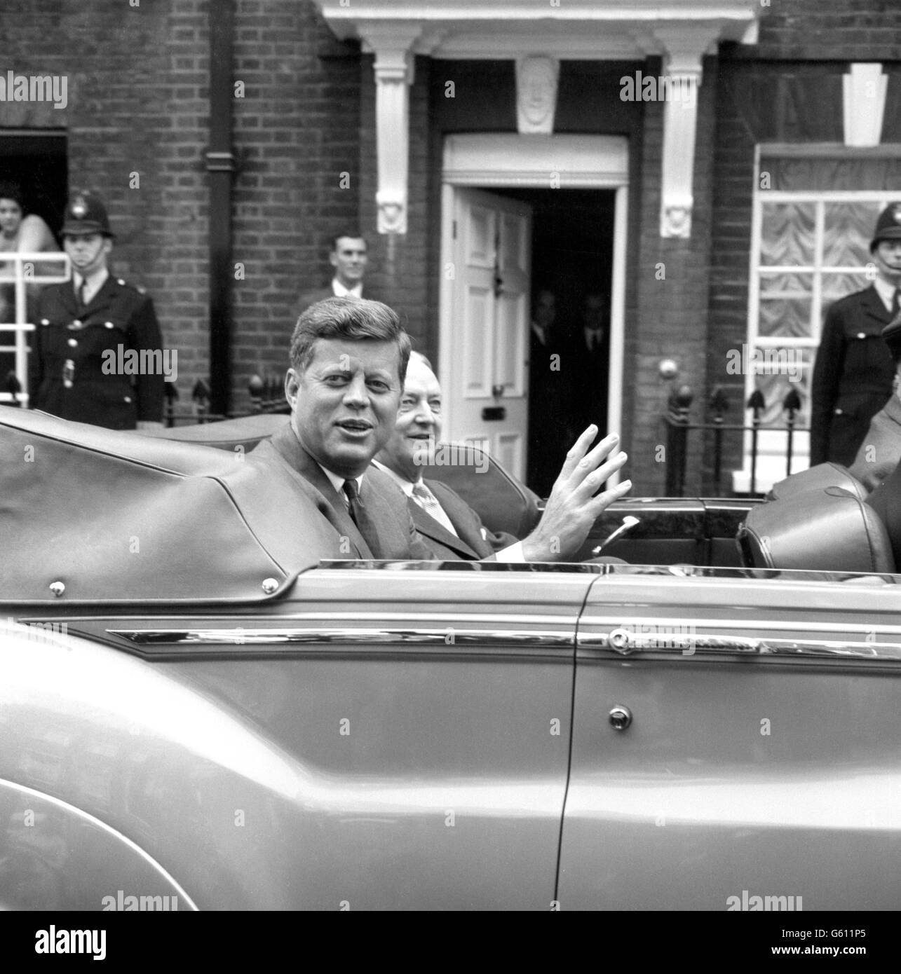 Präsident John Kennedy von Amerika winkt, als er in einem offenen Auto die Residenz seiner Schwägerin im Buckingham Palace zur US-Botschaft verlässt. Stockfoto