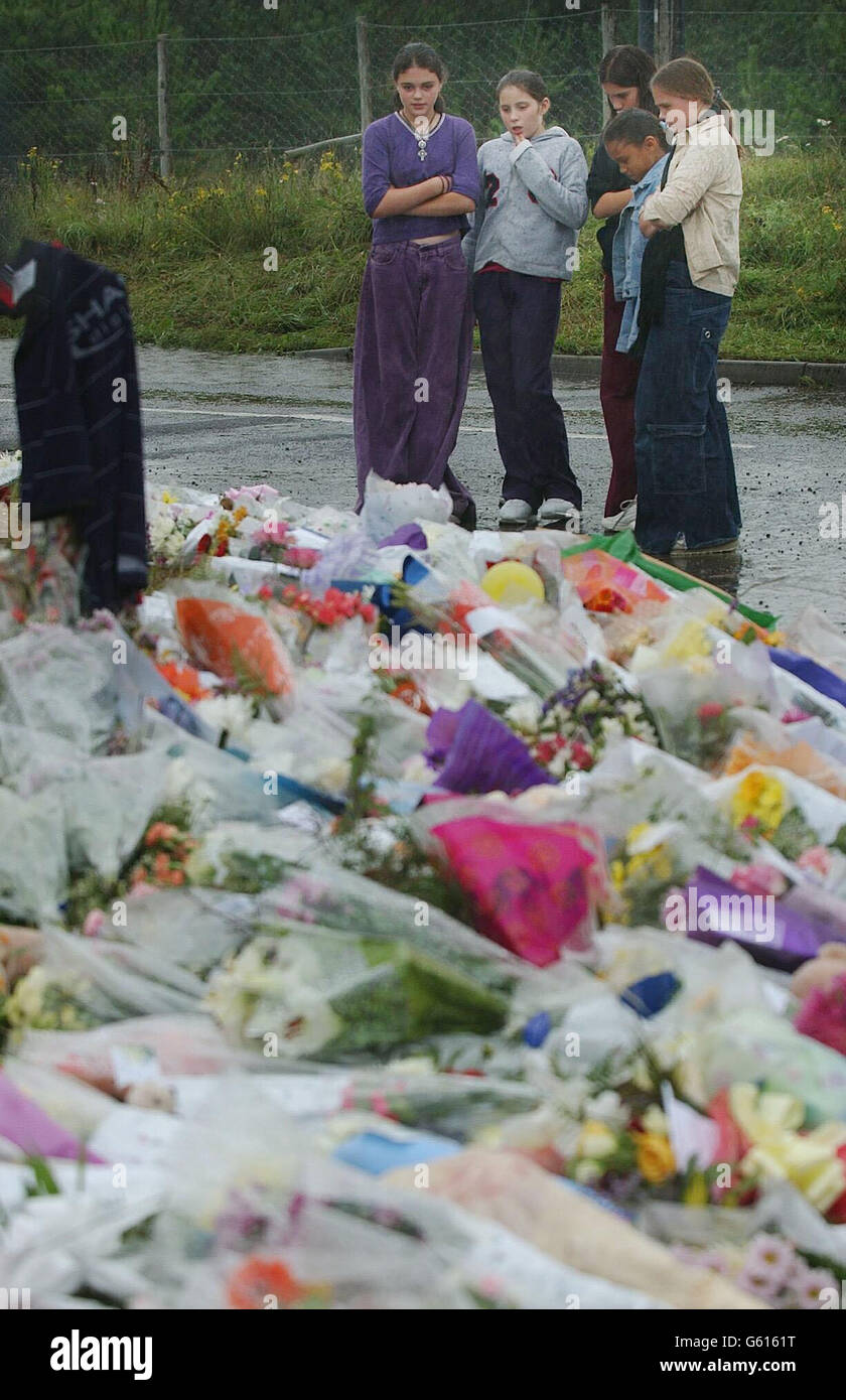 Wellwishers schauen sich Blumen an, die am Straßenrand zu Ehren von Holly Wells und Jessica Chapman hinterlassen wurden, mit dem Carr Woodland Nature Area im Hintergrund, wo forensische Teams der Polizei weiter suchen, in der Nähe von Lakenheath, Suffolk. *die Polizei, die den Tod der beiden Mädchen untersucht, stellt weiterhin einen Hausmeister und seine Freundin in Frage, die wegen des Verdachts ihres Mordes verhaftet wurde. Gestern Abend gewährten die Richter der Polizei von Cambridgeshire eine weitere und letzte Verlängerung um 36 Stunden, um Ian Huntley, 28, und seine Freundin Maxine Carr, 25, wegen der Morde an den beiden 10-Jährigen zu befragen. Stockfoto