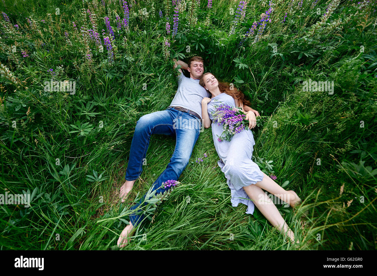 Mann und Frau umarmen, Gras auf einer Wiese mit Bouquet von Lupinen liegend Stockfoto