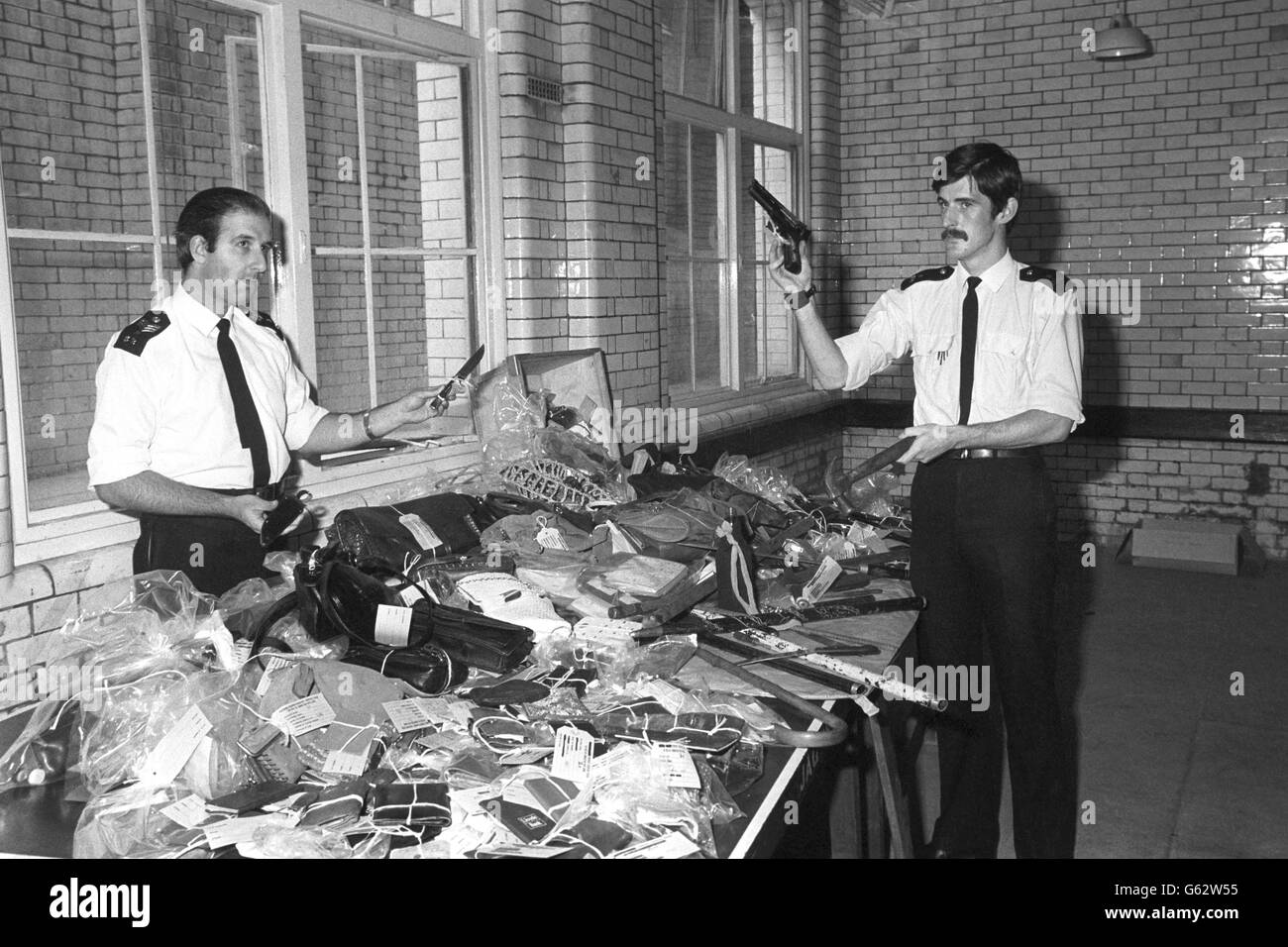 Sergeant Colin Levy (links) zeigt zwei der Messer und PC Sean Gleason zeigt eine Pistole und einen Hammer, die zu den gefährlichen Waffen gehörten, die auf der Straße gefunden wurden, nachdem Gewalt den Notting Hill Carnival in London plündert hatte. Die Gegenstände werden auf der Notting Hill Polizeistation als verlorenes Eigentum aufgeführt, aber sie erwarten, dass sie nicht beansprucht werden. Stockfoto