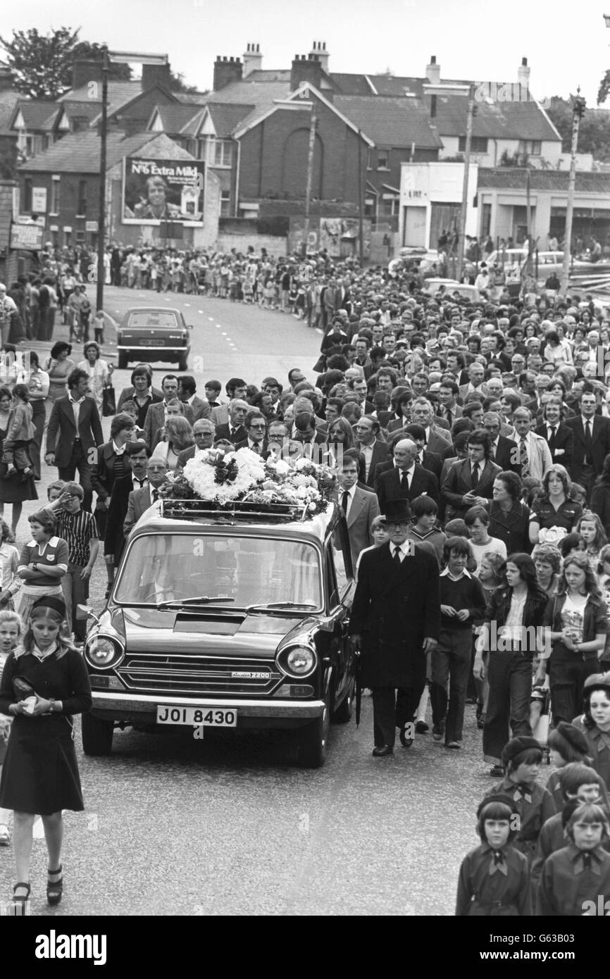 Trauernde Trauernde laufen hinter den Leichenwagen und tragen die Särge der drei jungen Maguire-Kinder, die von einem auslaufenden Auto getötet wurden, während der Trauerprozession von der römisch-katholischen Kirche in der Finnaghy Road North zum Milltown-Friedhof in Belfast. Geschäfte, Bars und Fabriken schlossen, als Arbeiter die 1,000 starke Prozession beobachteten. Menschenmengen wurden auf 5,000 Menschen geschätzt. Stockfoto